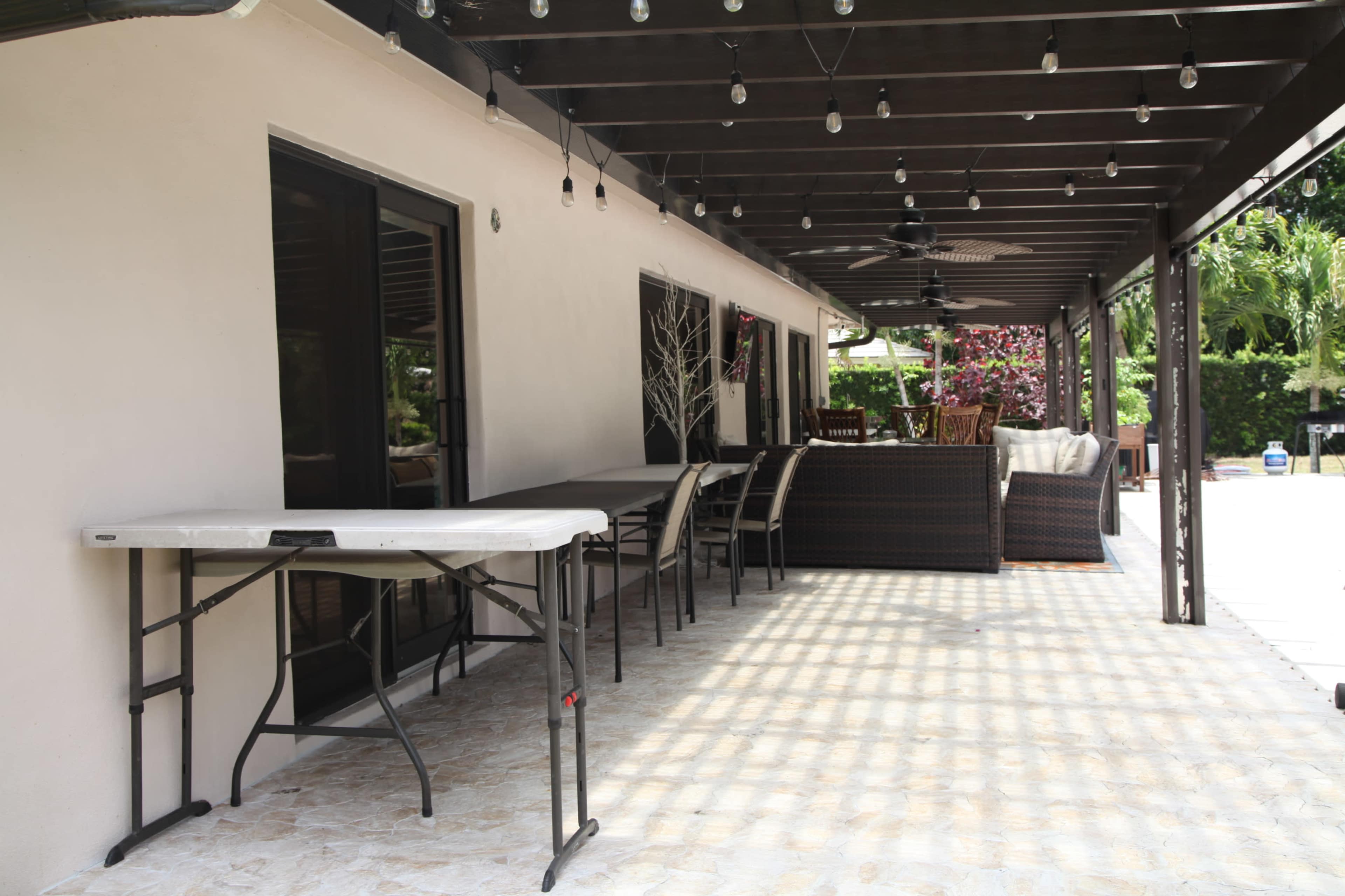 A covered patio area with a folding table and several seating arrangements, illuminated by string lights overhead.