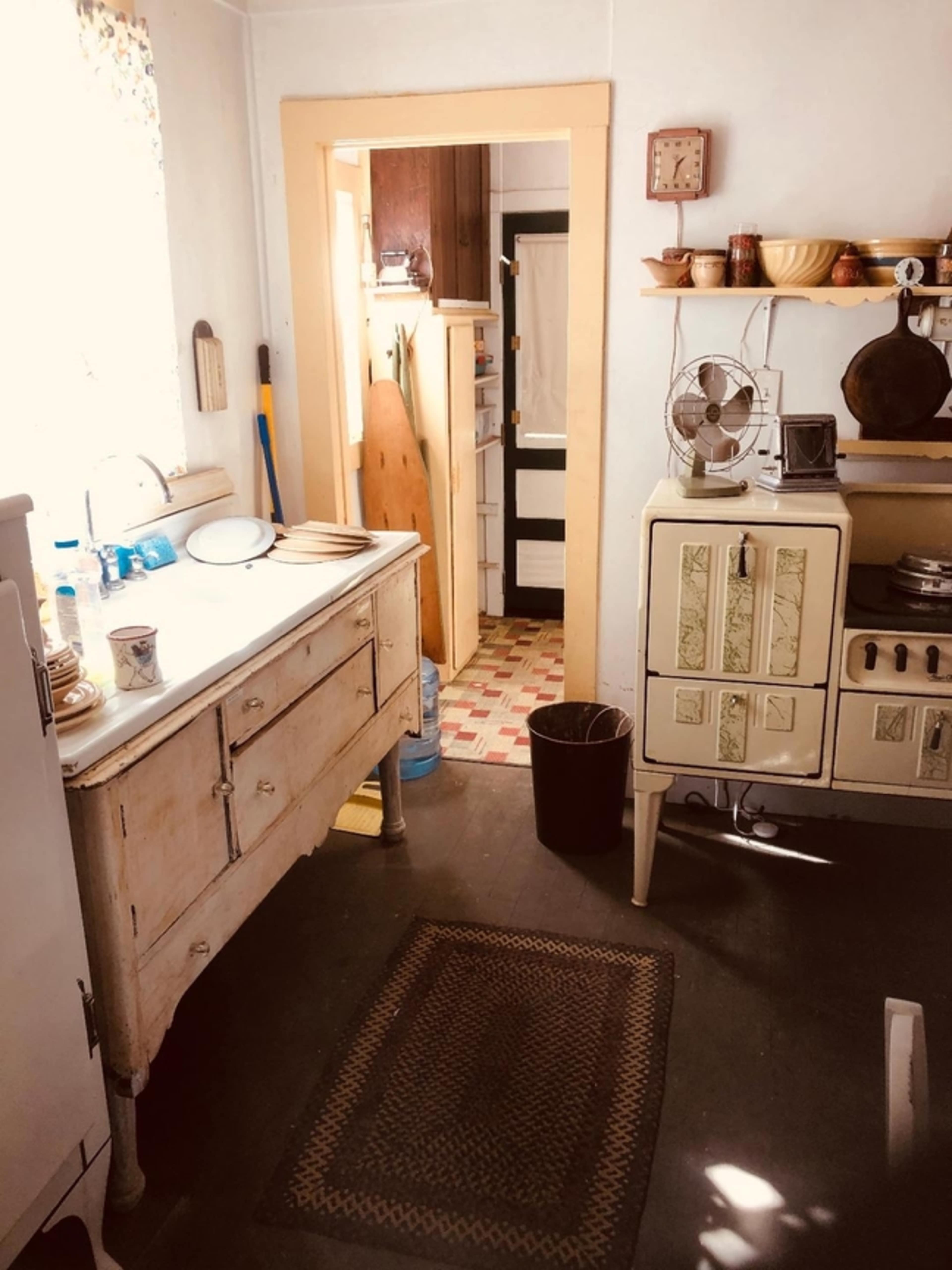 A rustic kitchen with an antique sink and stove, along with a door leading to a hallway.