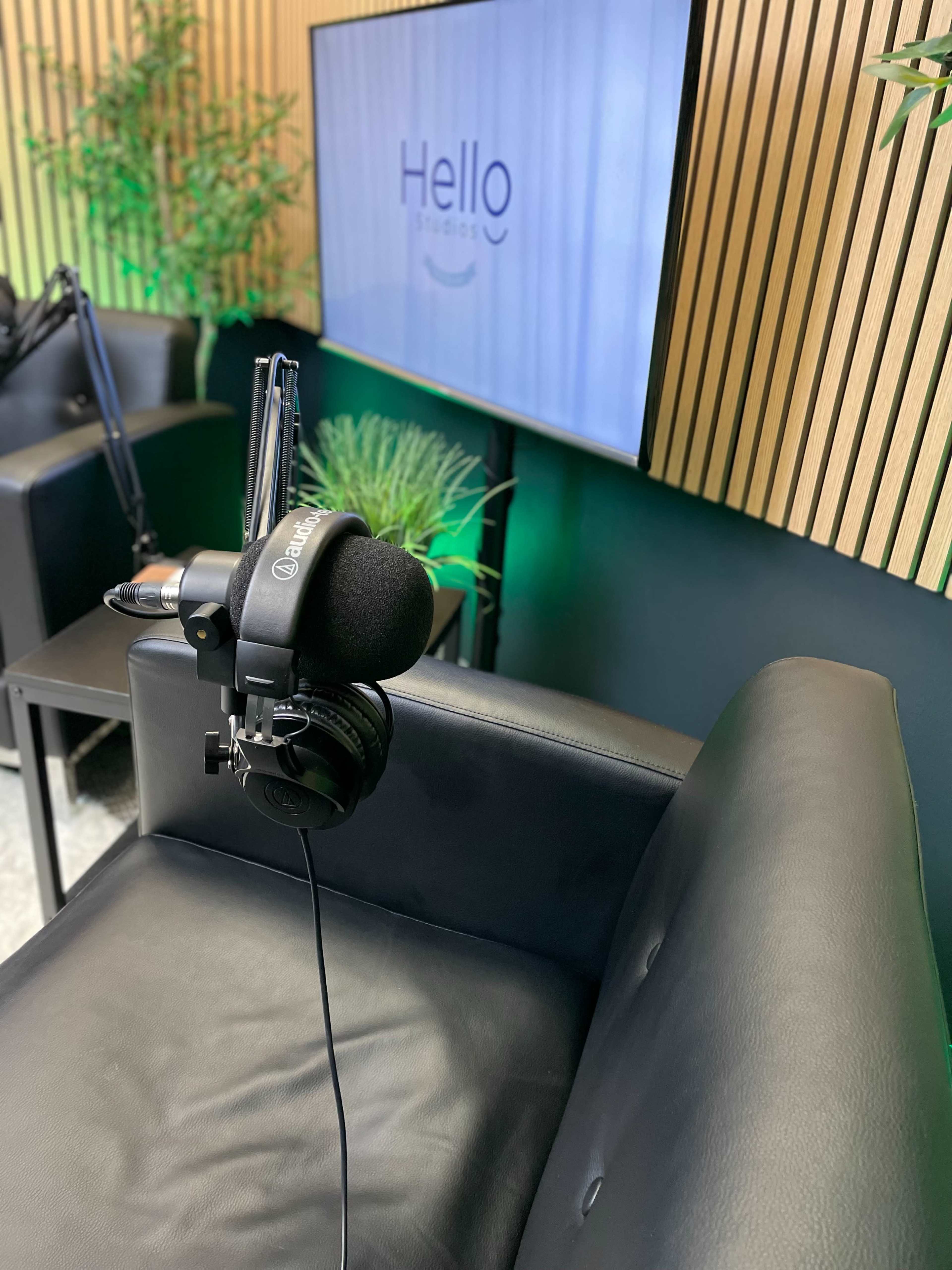 A microphone with headphones is positioned on a black chair in front of a screen displaying the text "Hello" in a modern studio setting.