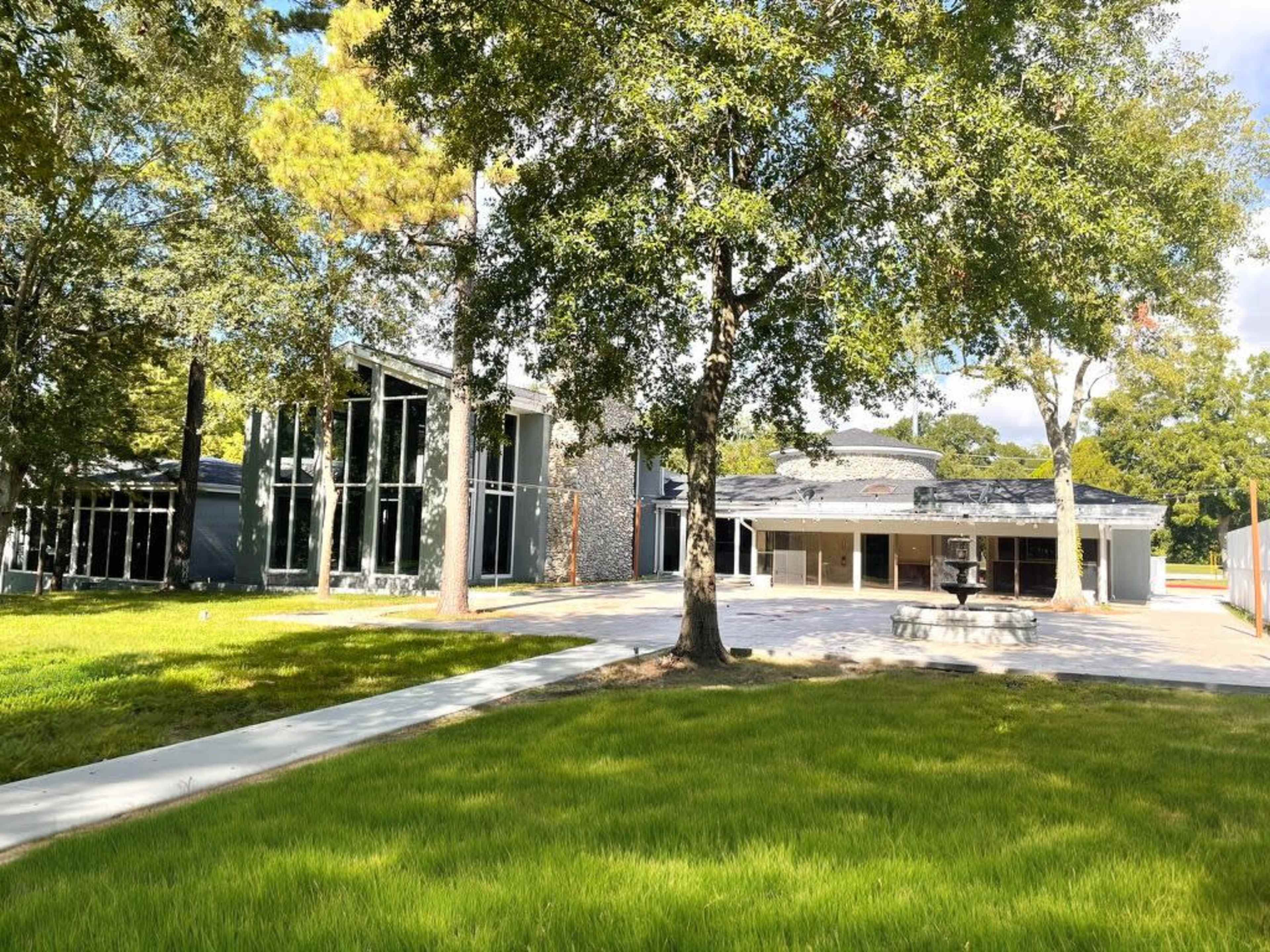 The image shows a modern building surrounded by trees and a manicured lawn.