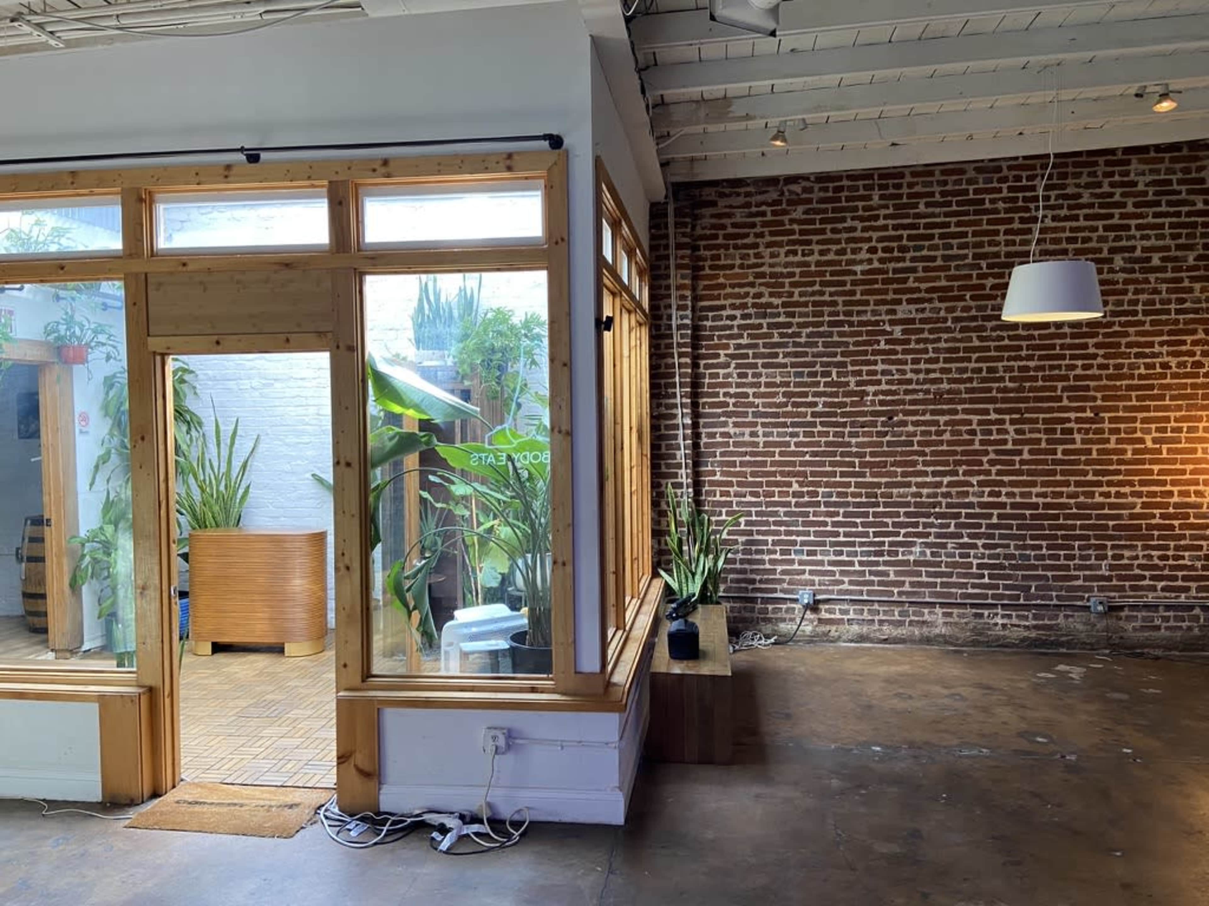 A spacious room with a wooden-framed glass entrance to a plant-filled area on the left and a brick wall on the right.