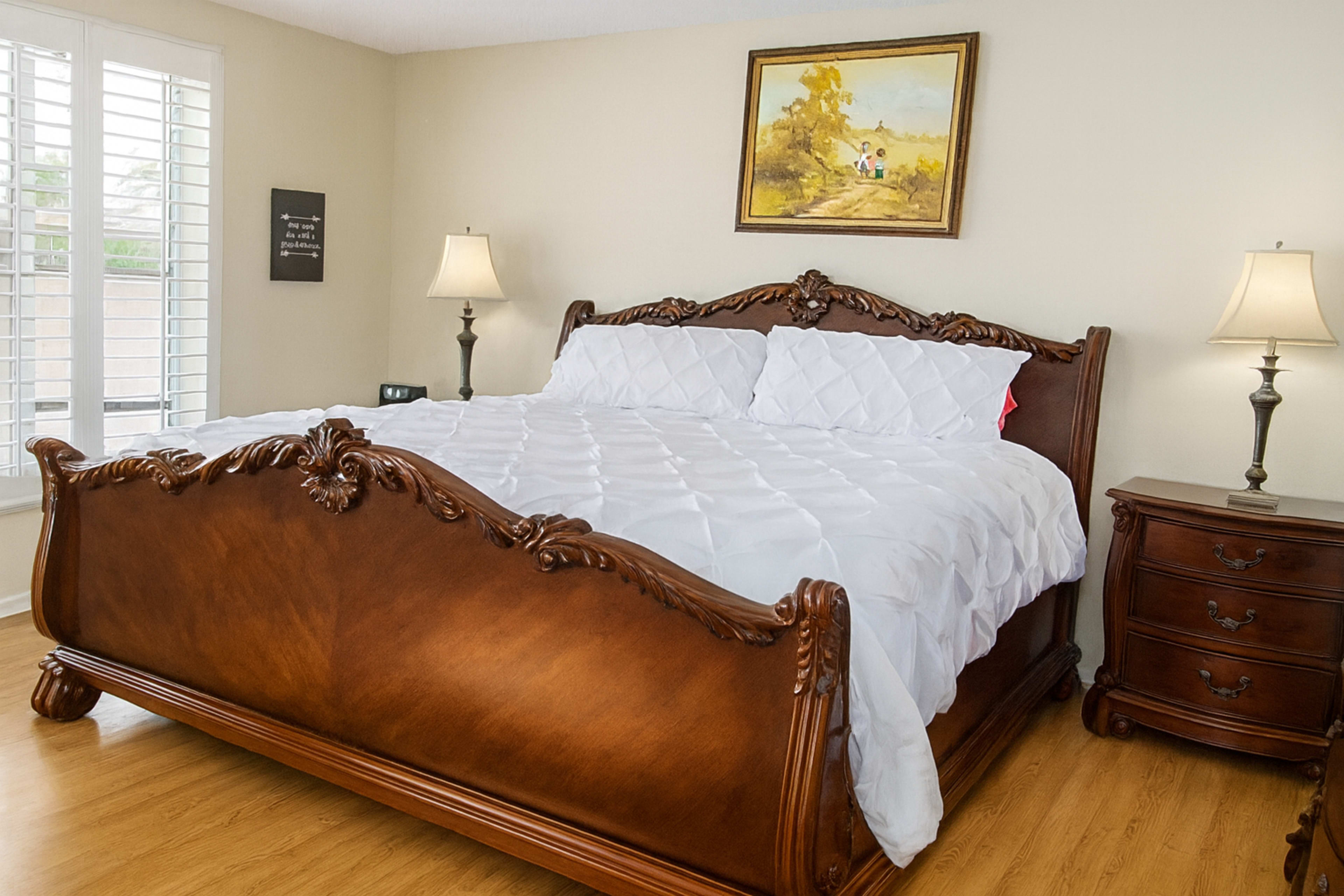 The image shows a well-decorated bedroom with a wooden bed, white bedding, a nightstand, and two lamps.