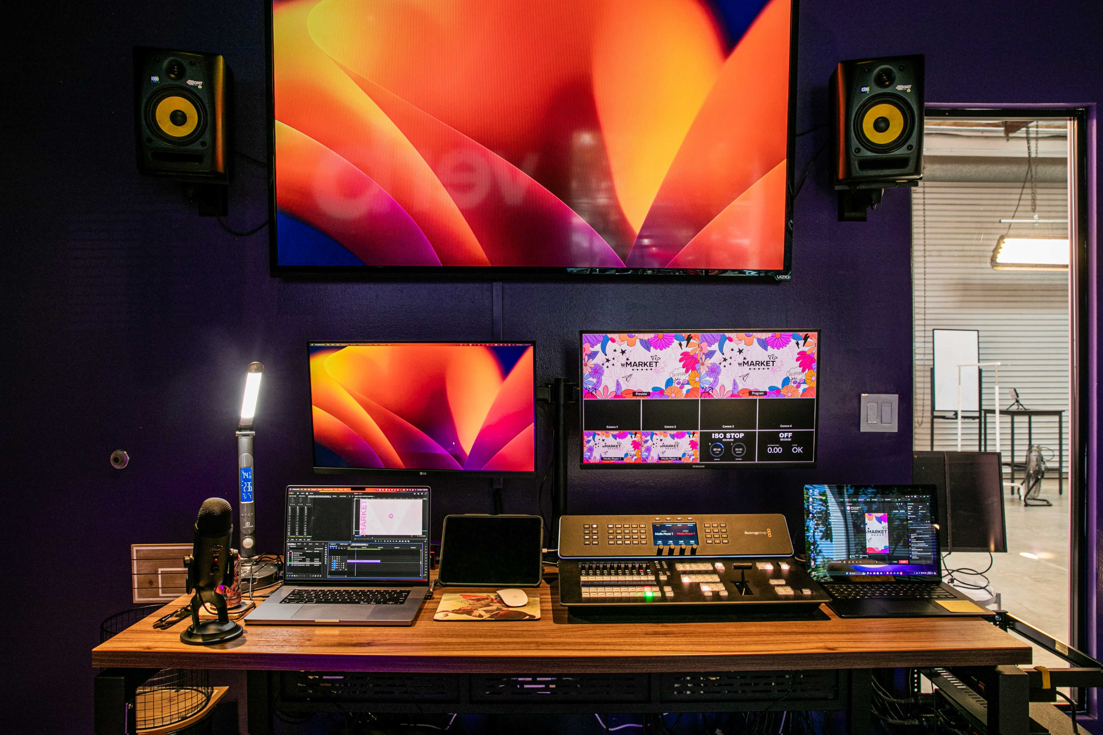 A media production setup featuring multiple monitors, a control panel, and various devices on a wooden table.