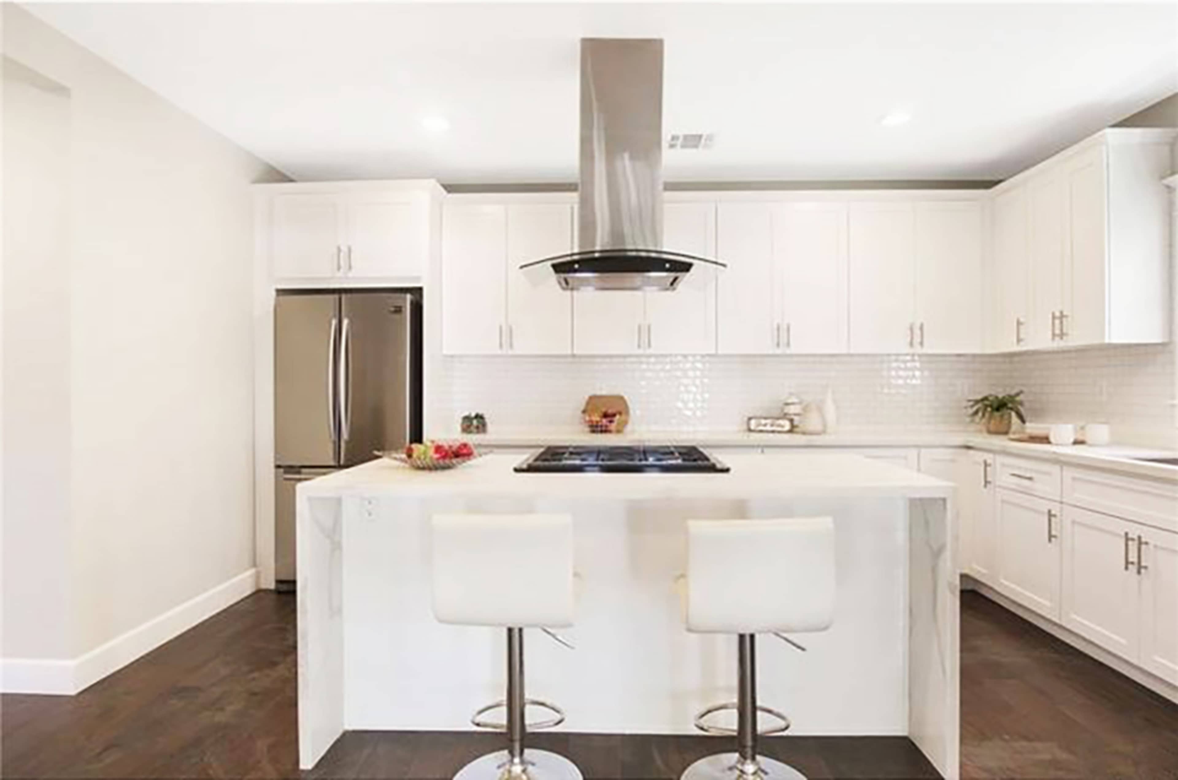 A modern kitchen features white cabinetry, stainless steel appliances, and a central island with two stools.