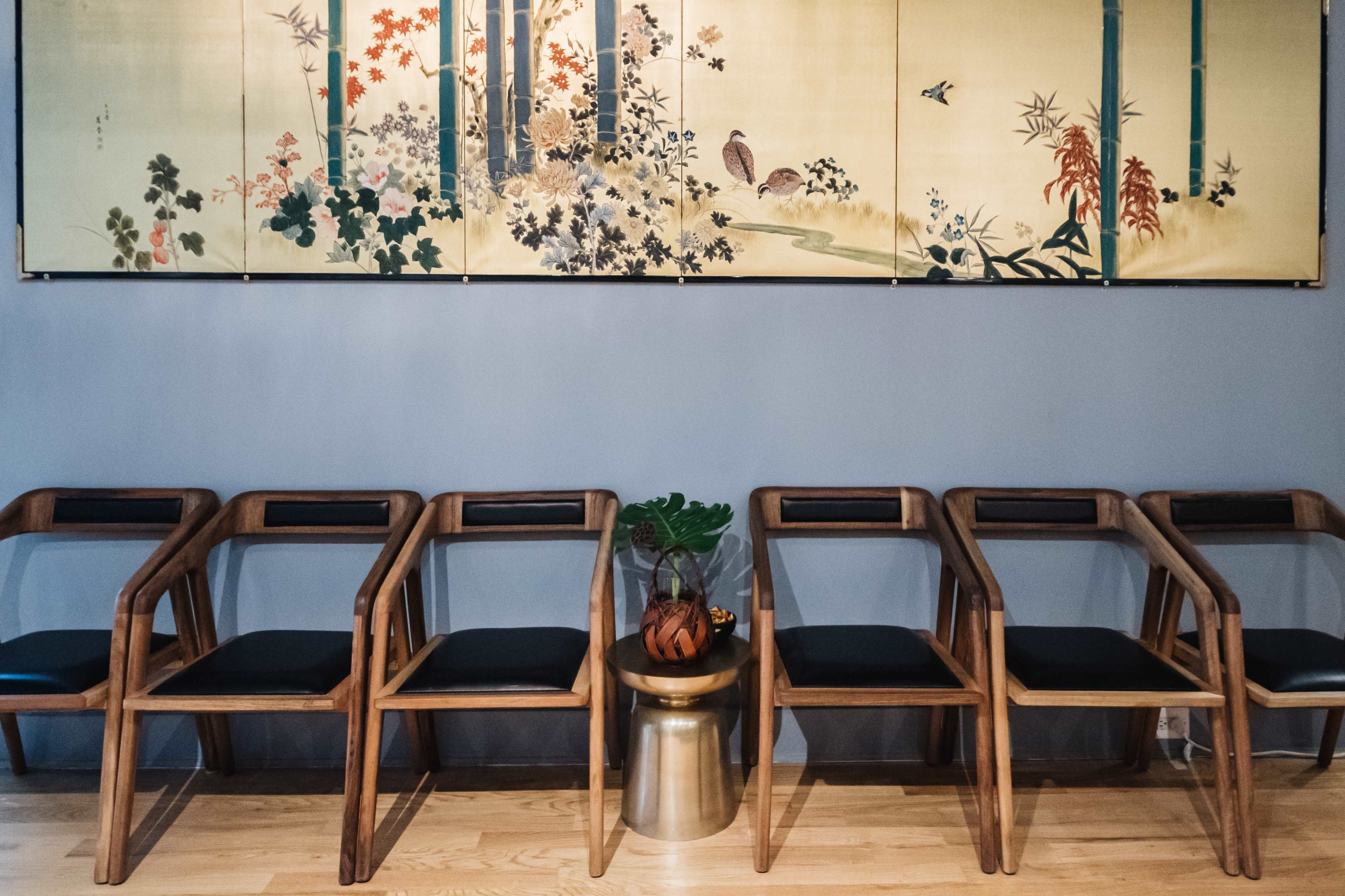 A row of wooden chairs beside a decorative wall covered with a painted scene of flowers and bamboo.