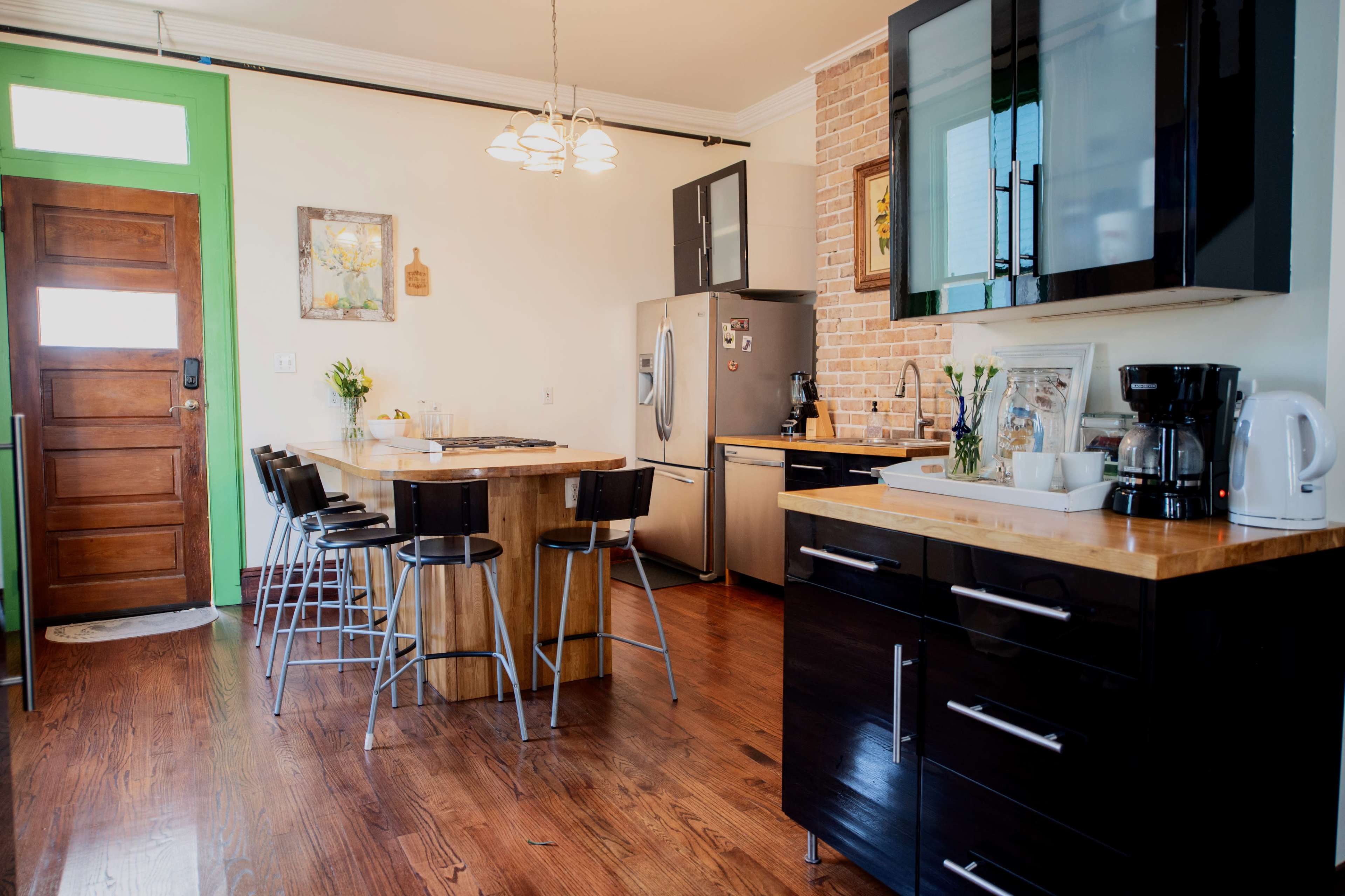 The image shows a modern kitchen featuring a wooden dining table and bar stools, stainless steel appliances, and a combination of dark and light cabinetry.