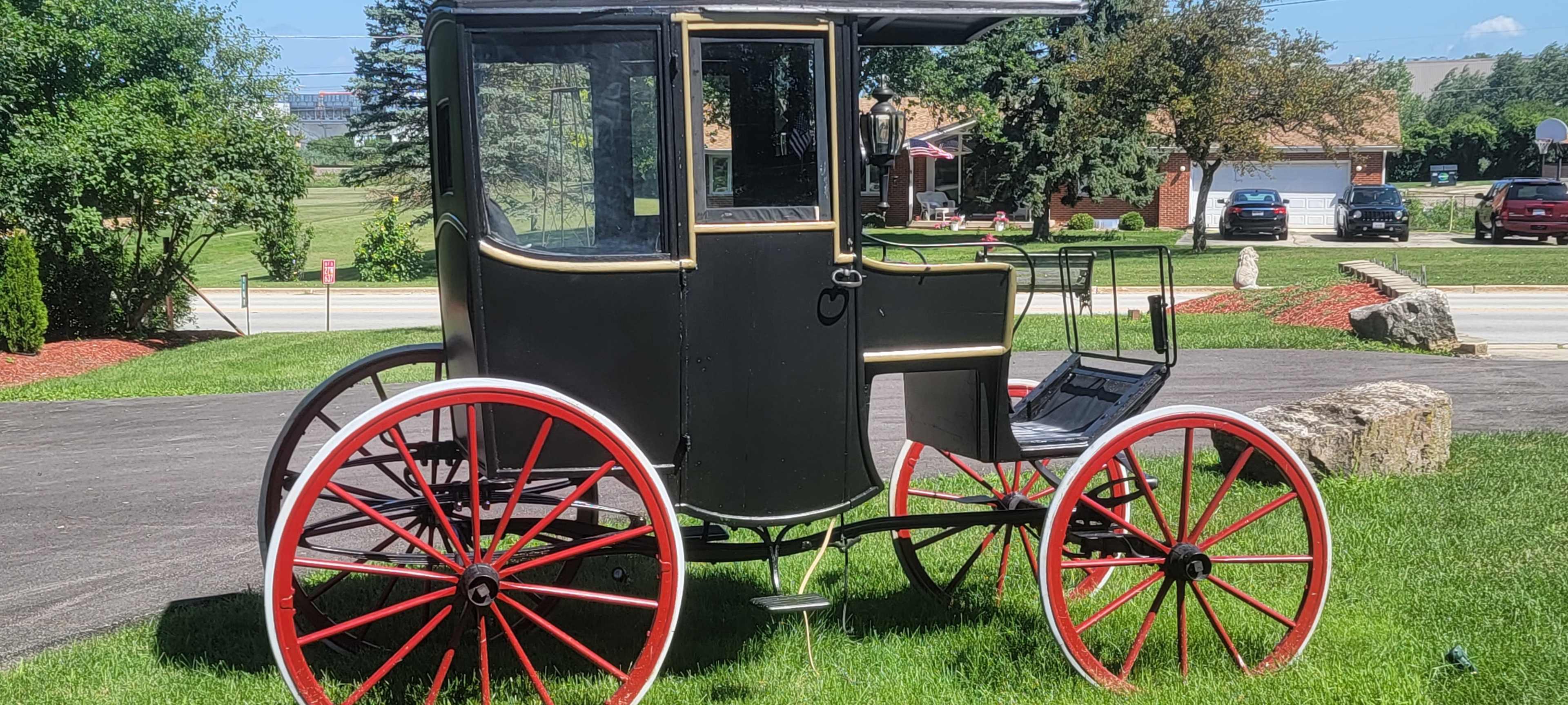 A vintage horse-drawn carriage parked on a grassy area near a roadway.