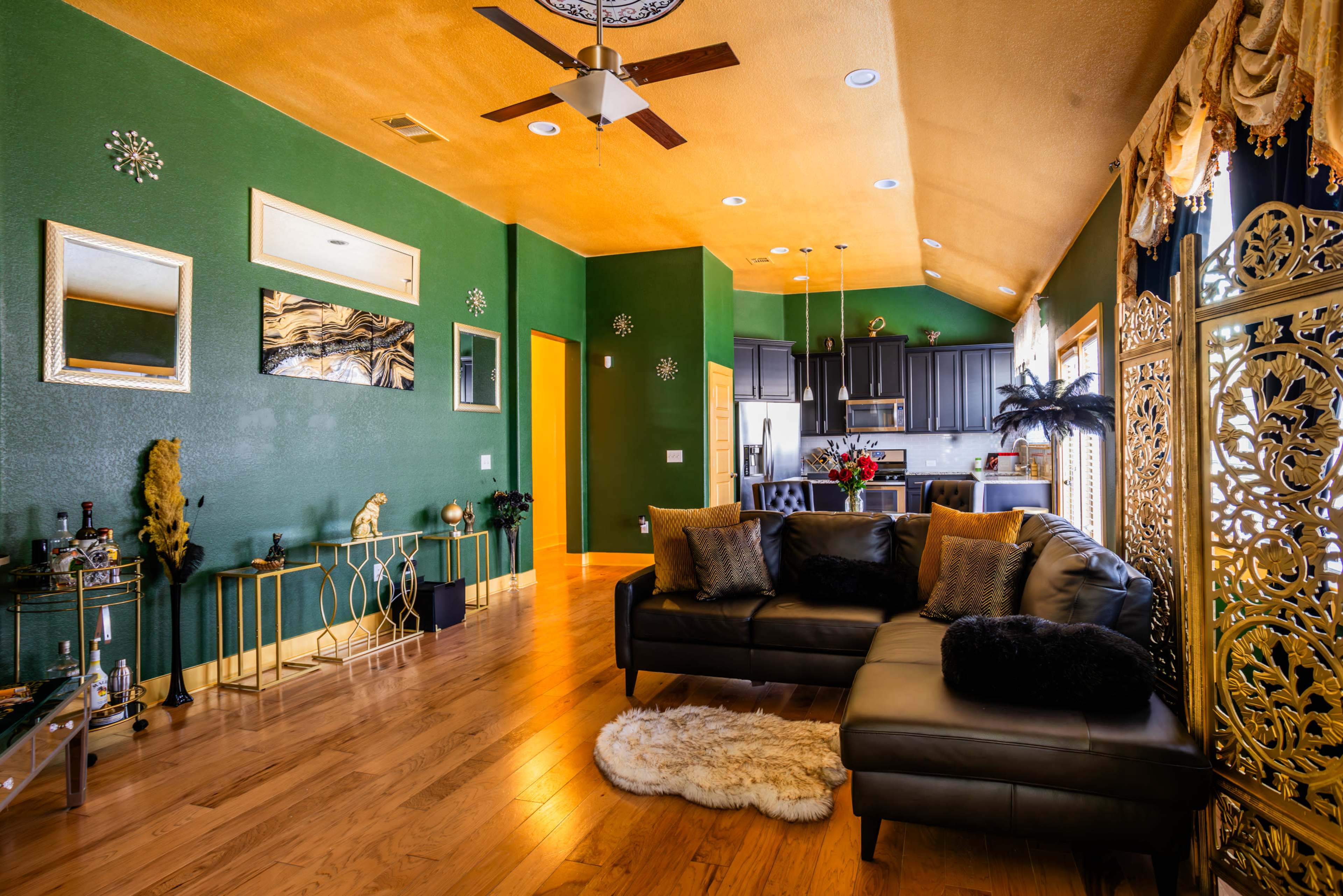 A modern living room with green walls, wooden flooring, and a dark sectional sofa, featuring decorative elements and plants.