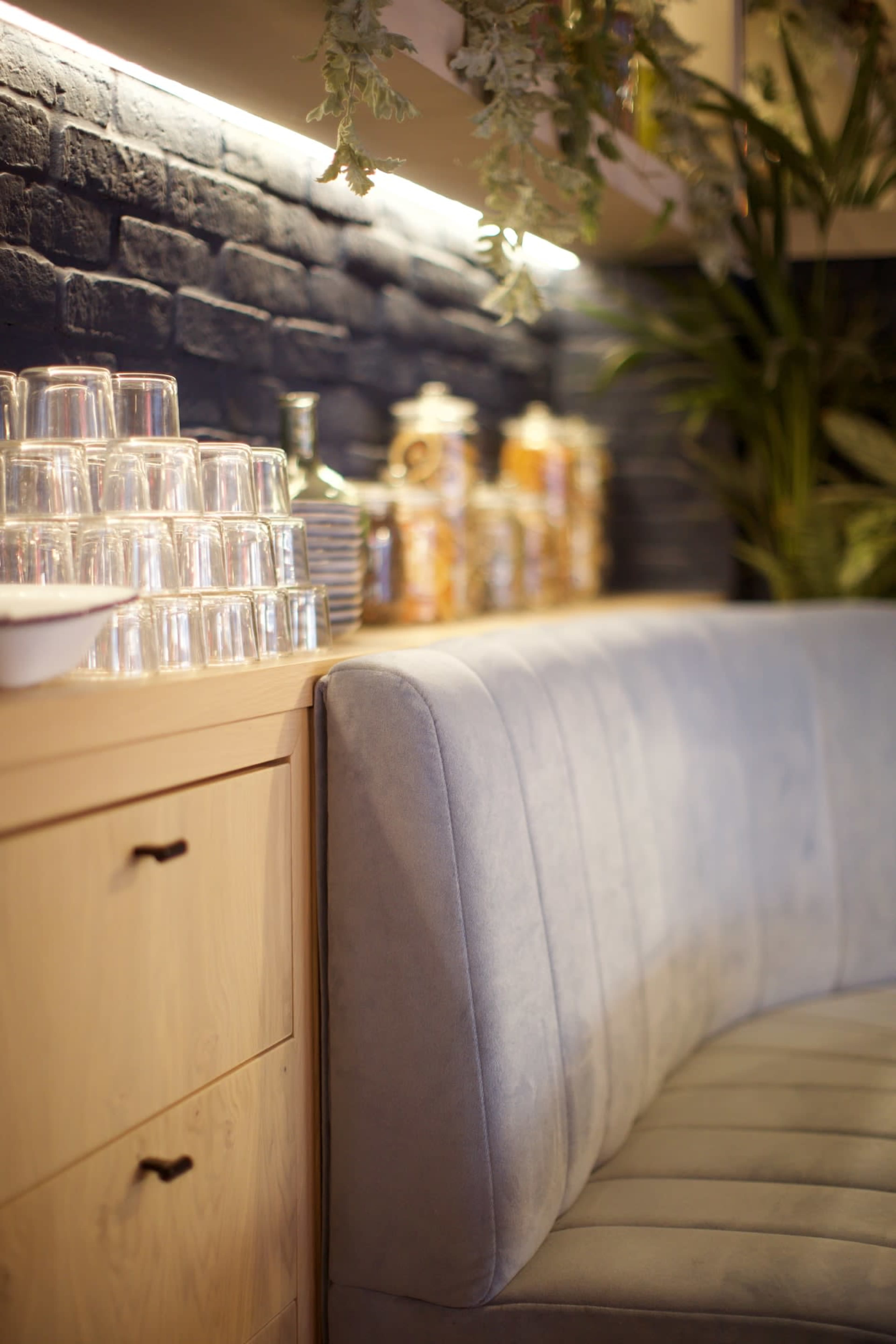 A curved gray sofa beside a wooden cabinet stacked with clear cups and various jars.