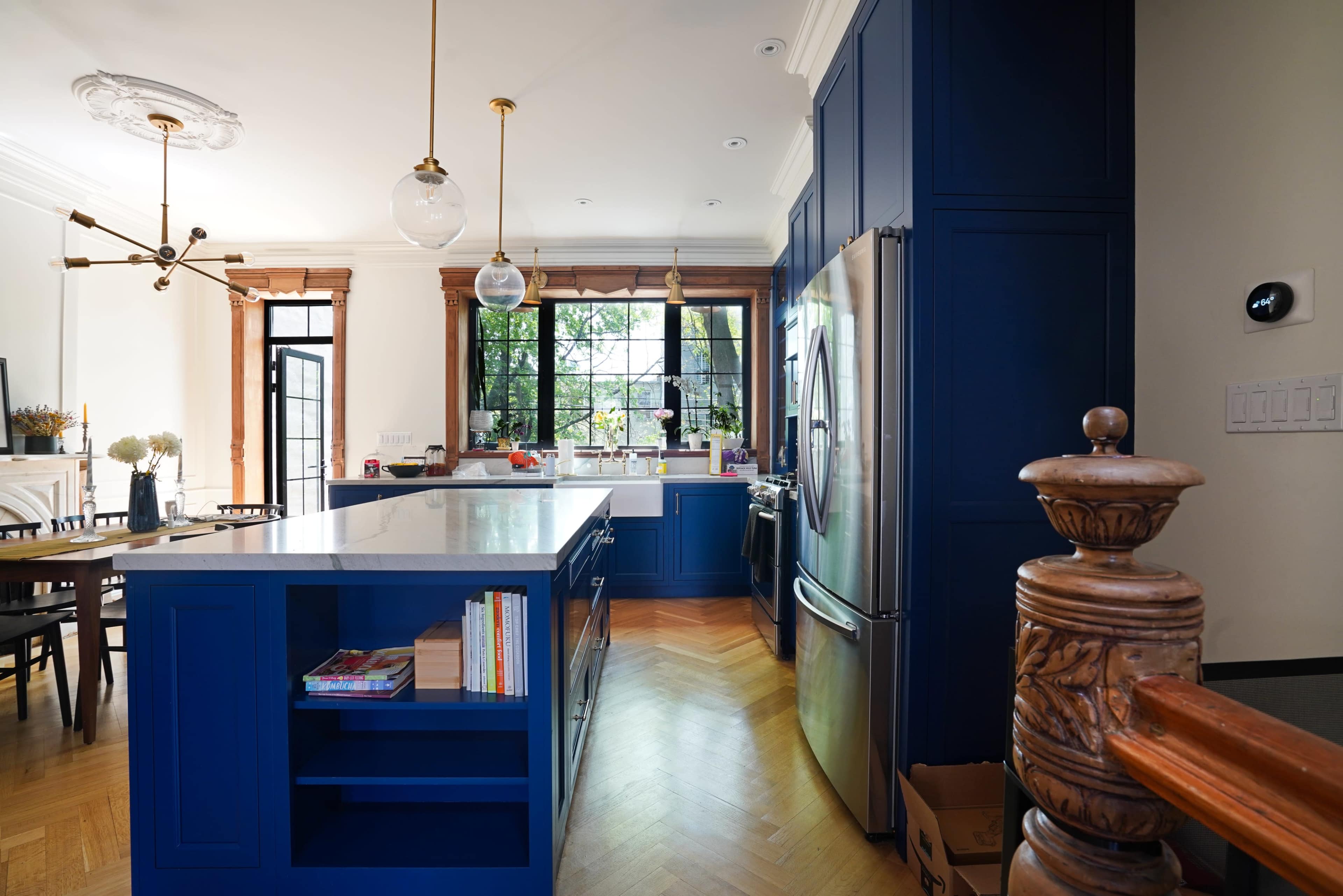 A modern kitchen features blue cabinetry, a central island with seating, and a view of an outdoor space through large windows.