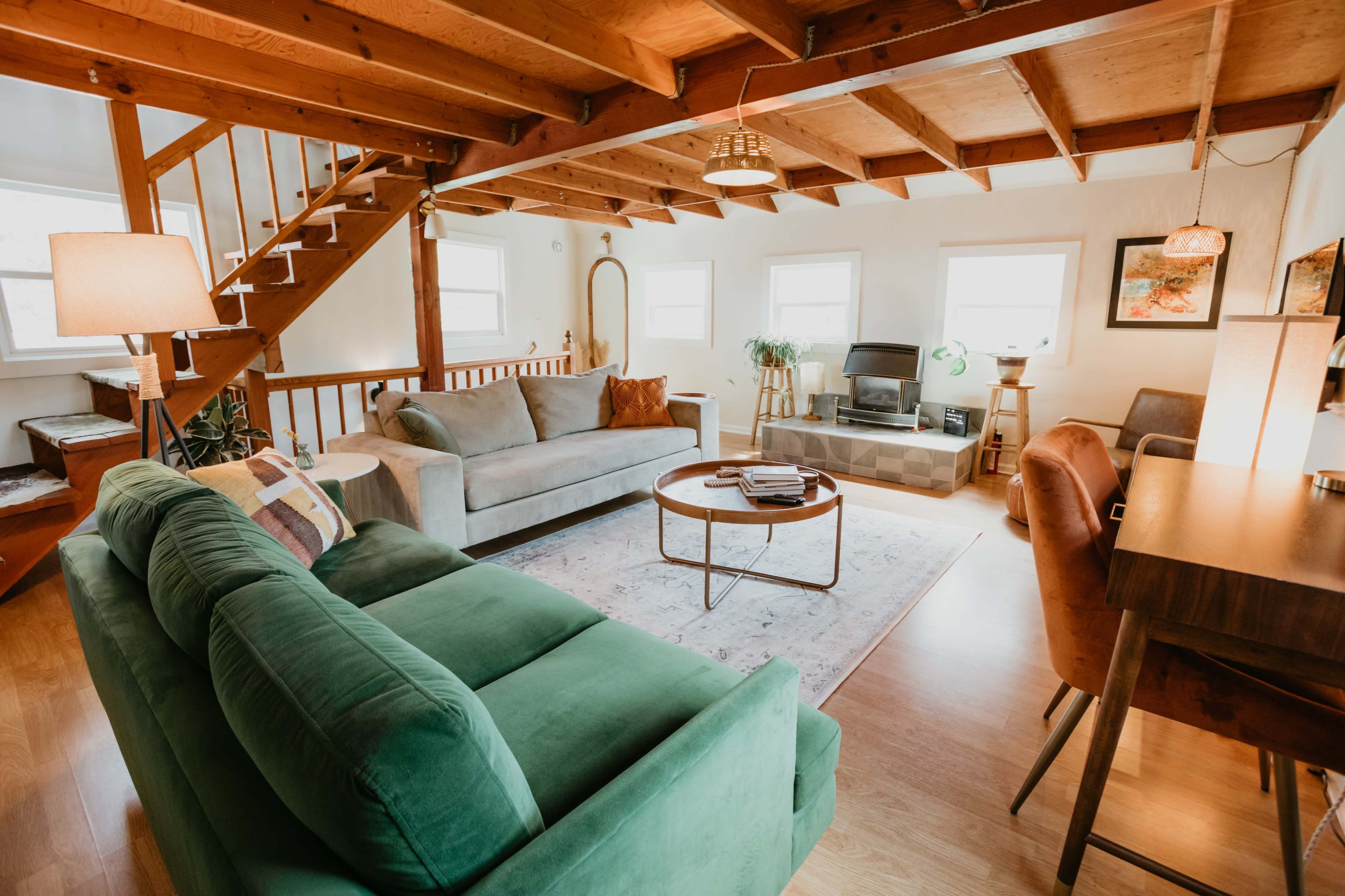 A spacious living room with green and gray sofas, a round coffee table, and a dining area, all under a wooden ceiling with exposed beams.