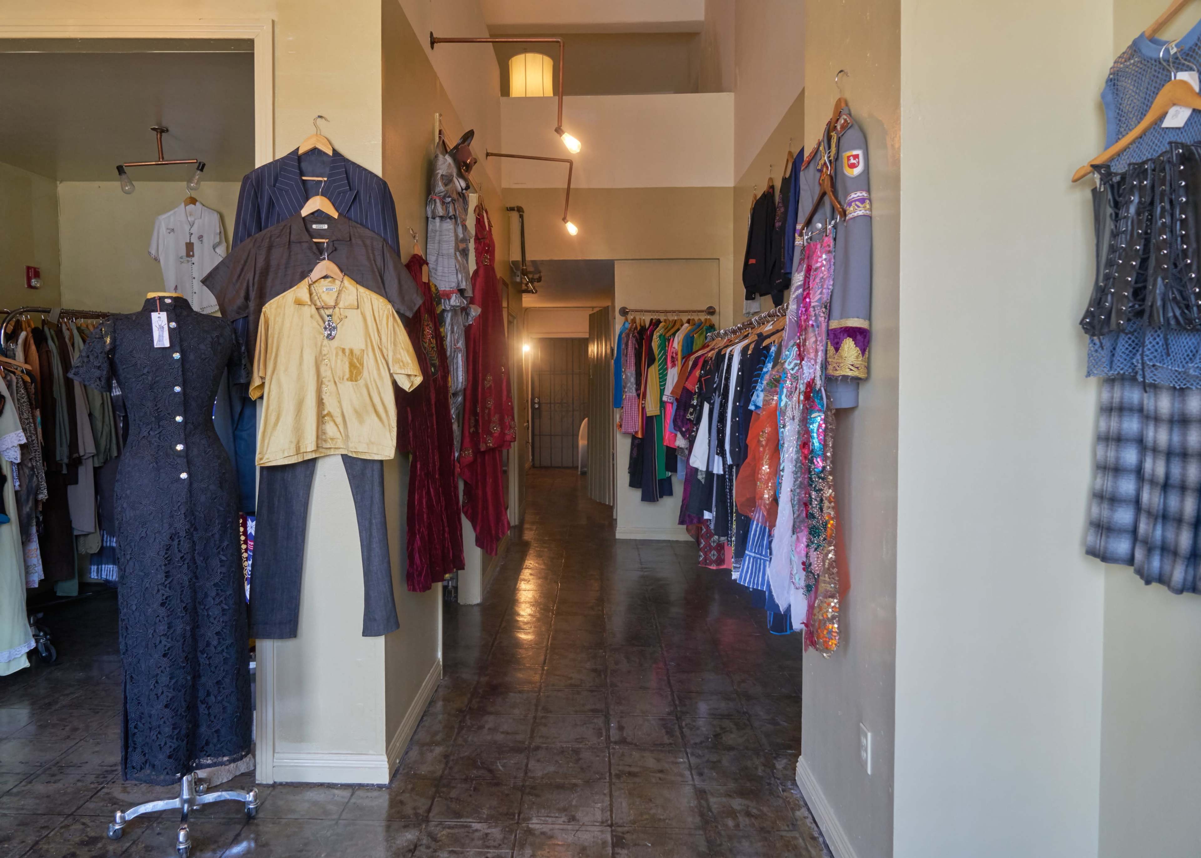A narrow clothing store aisle lined with various garments on hangers along both sides.