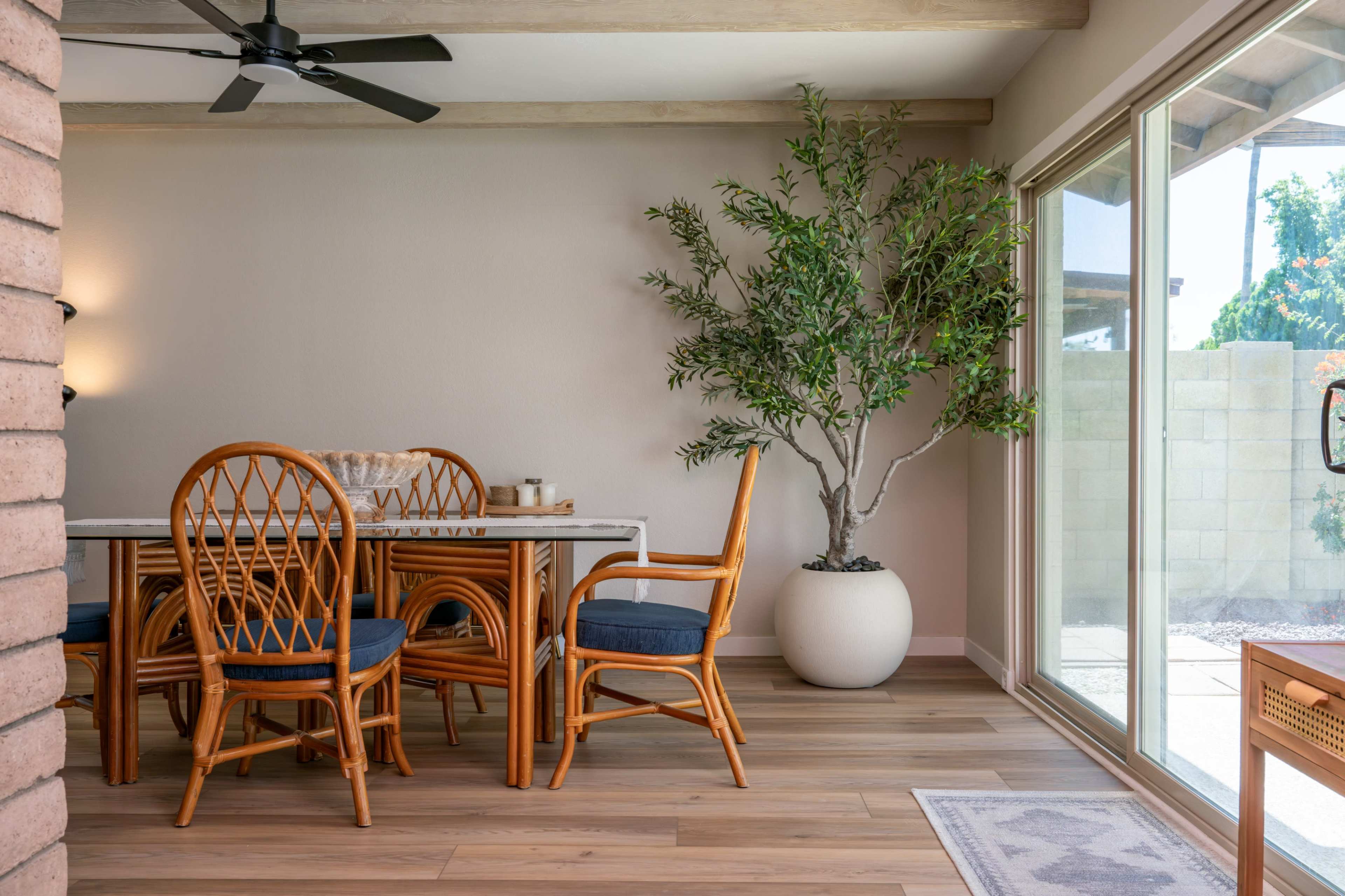 A dining area features a wicker table and chairs with a large potted plant beside a sliding glass door.