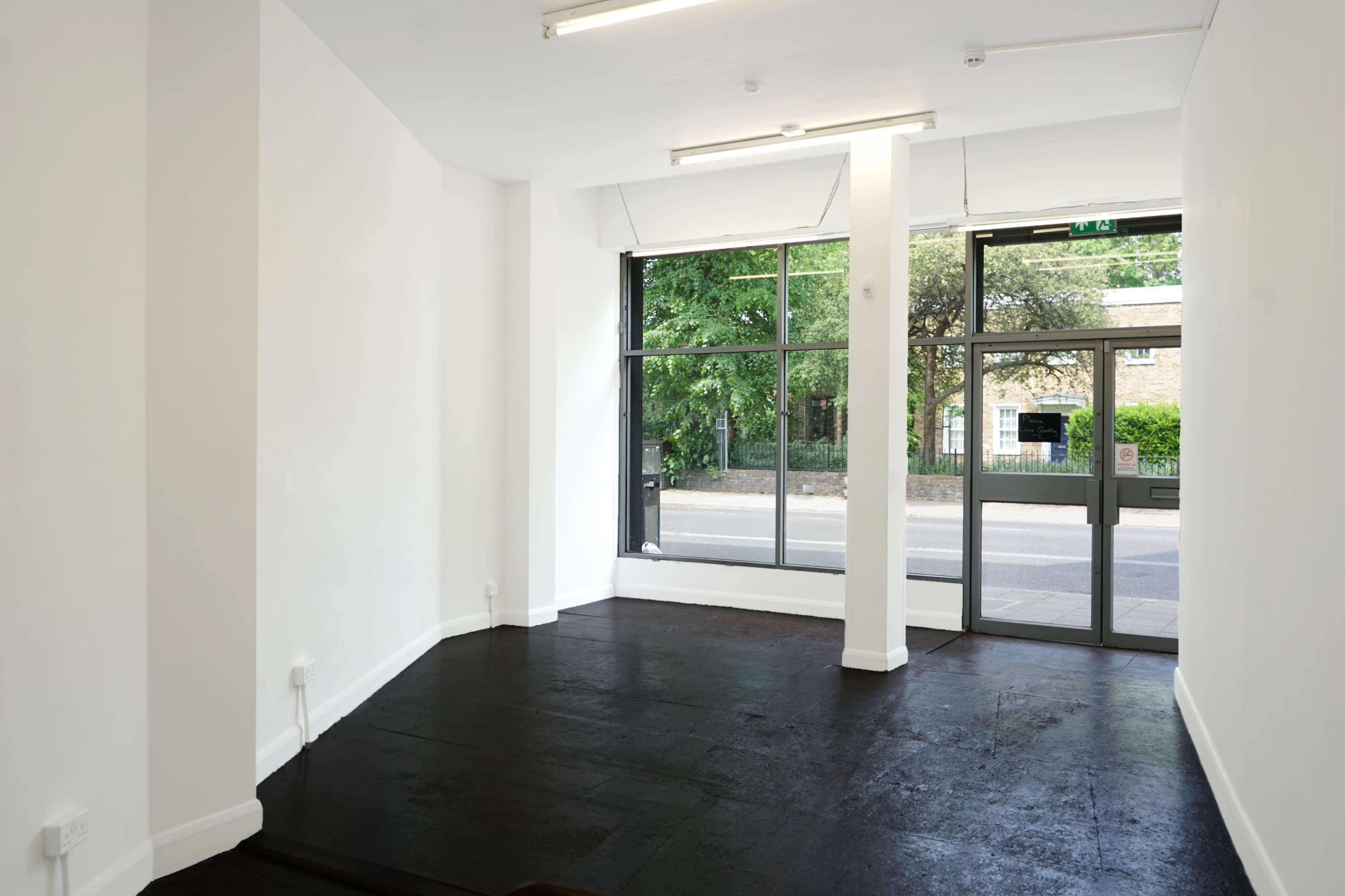 The image shows a spacious, empty room with a large front window and a door leading to the outside.