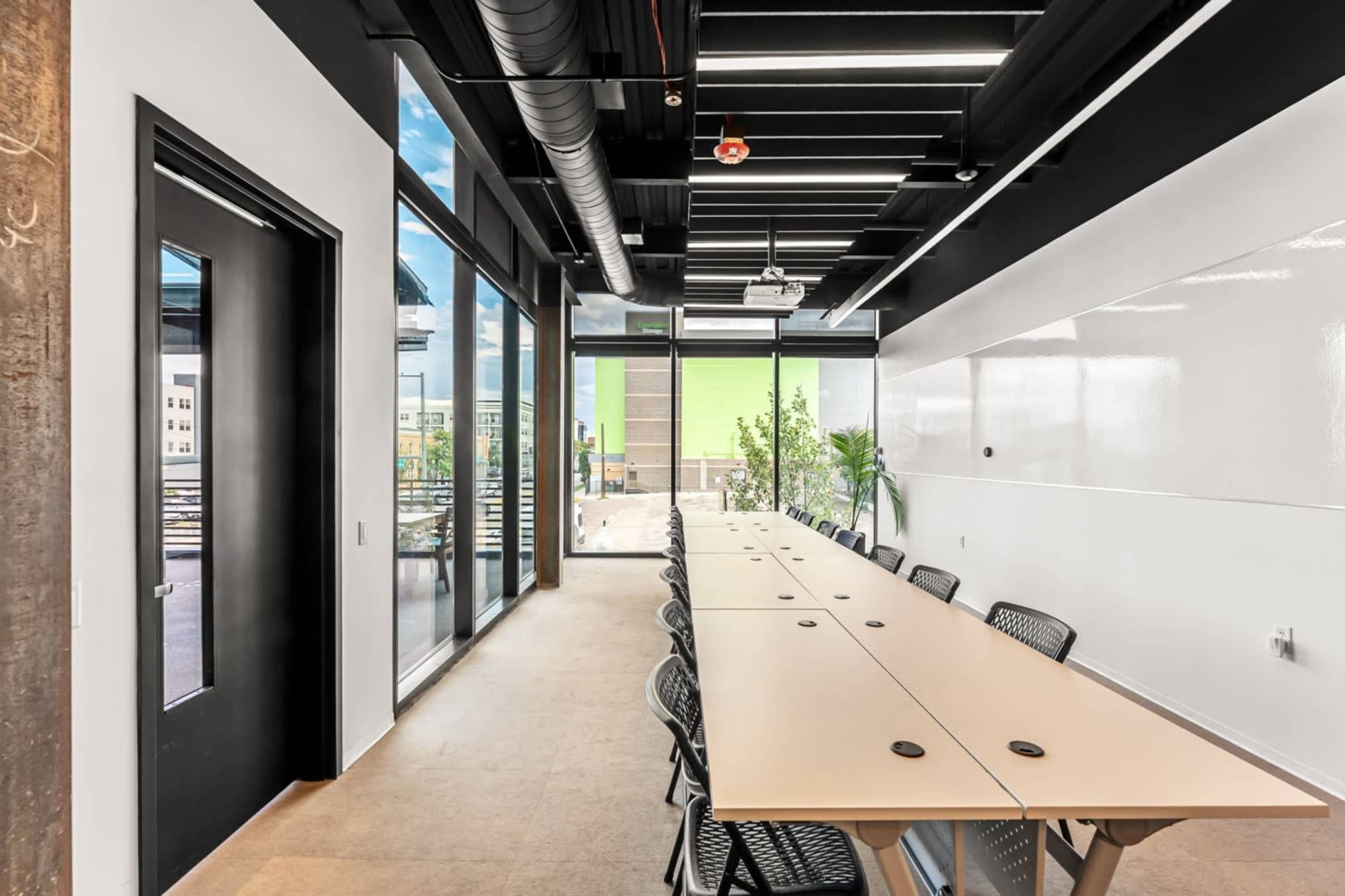 A spacious conference room features a long table with several chairs and large windows that provide natural light and a view of an outdoor area.