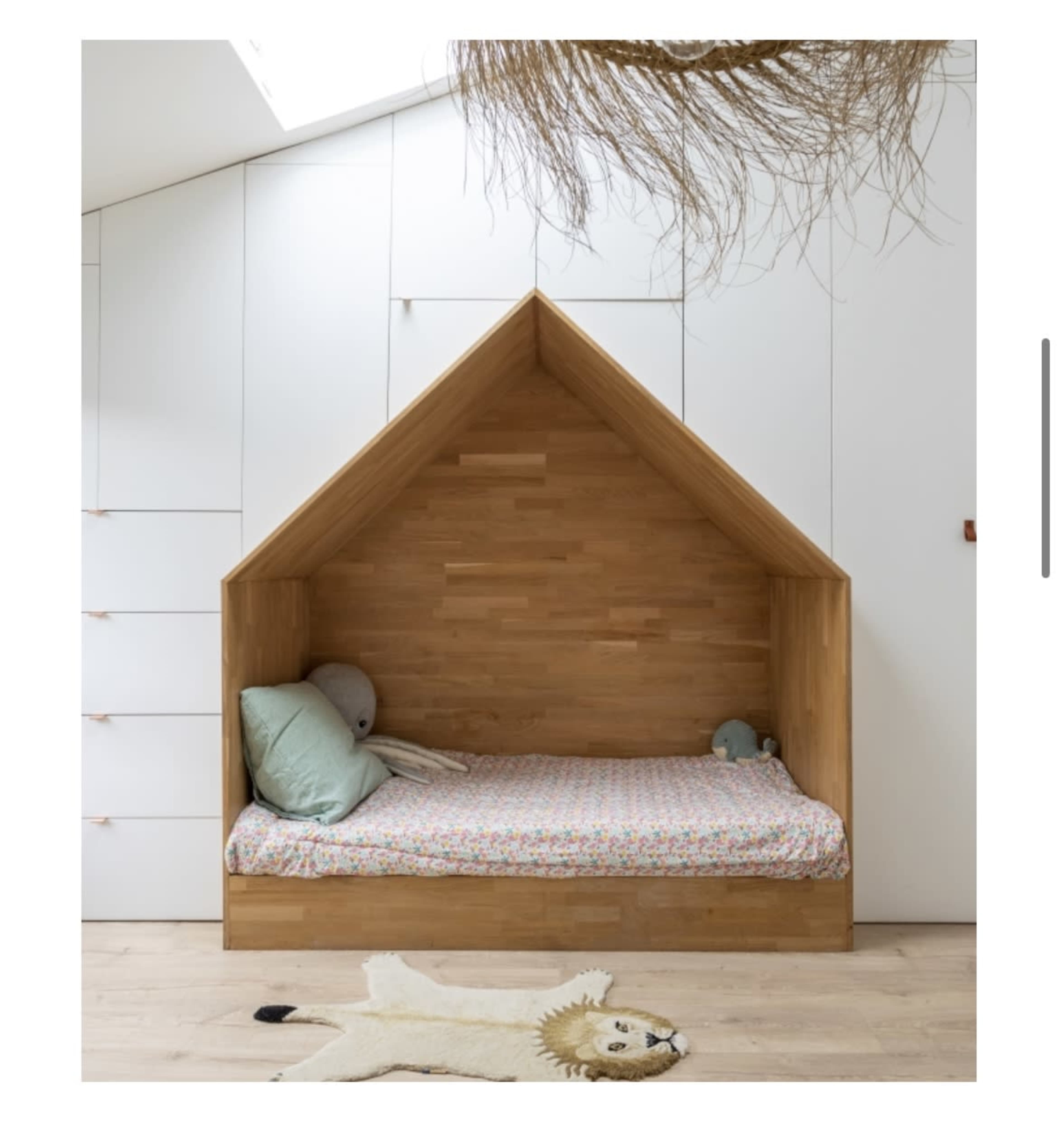 A wooden bed designed like a house, located against a white wall with storage drawers.