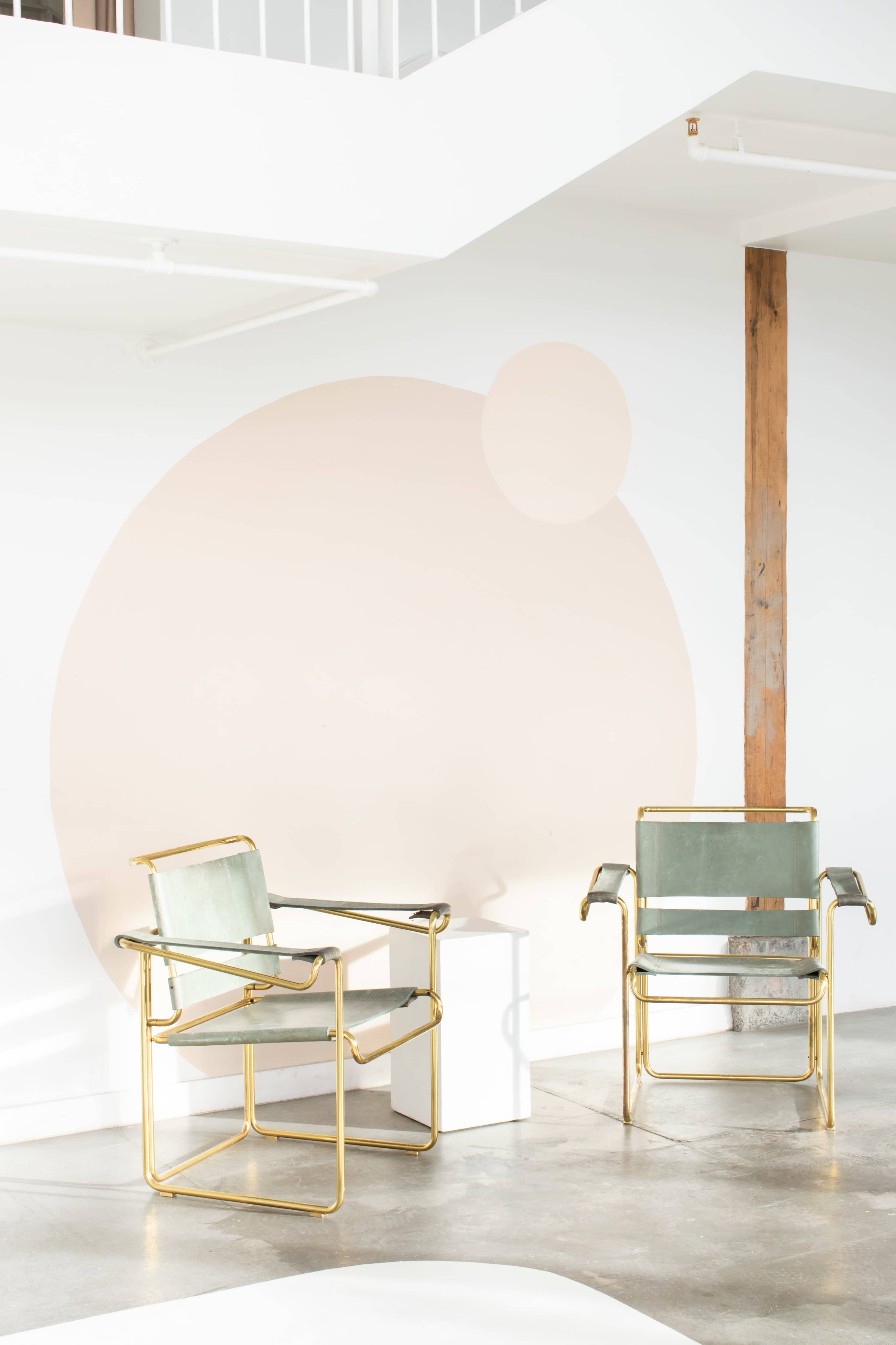 Two modern metal chairs with green upholstery are positioned near a white wall featuring a large pale circular design.