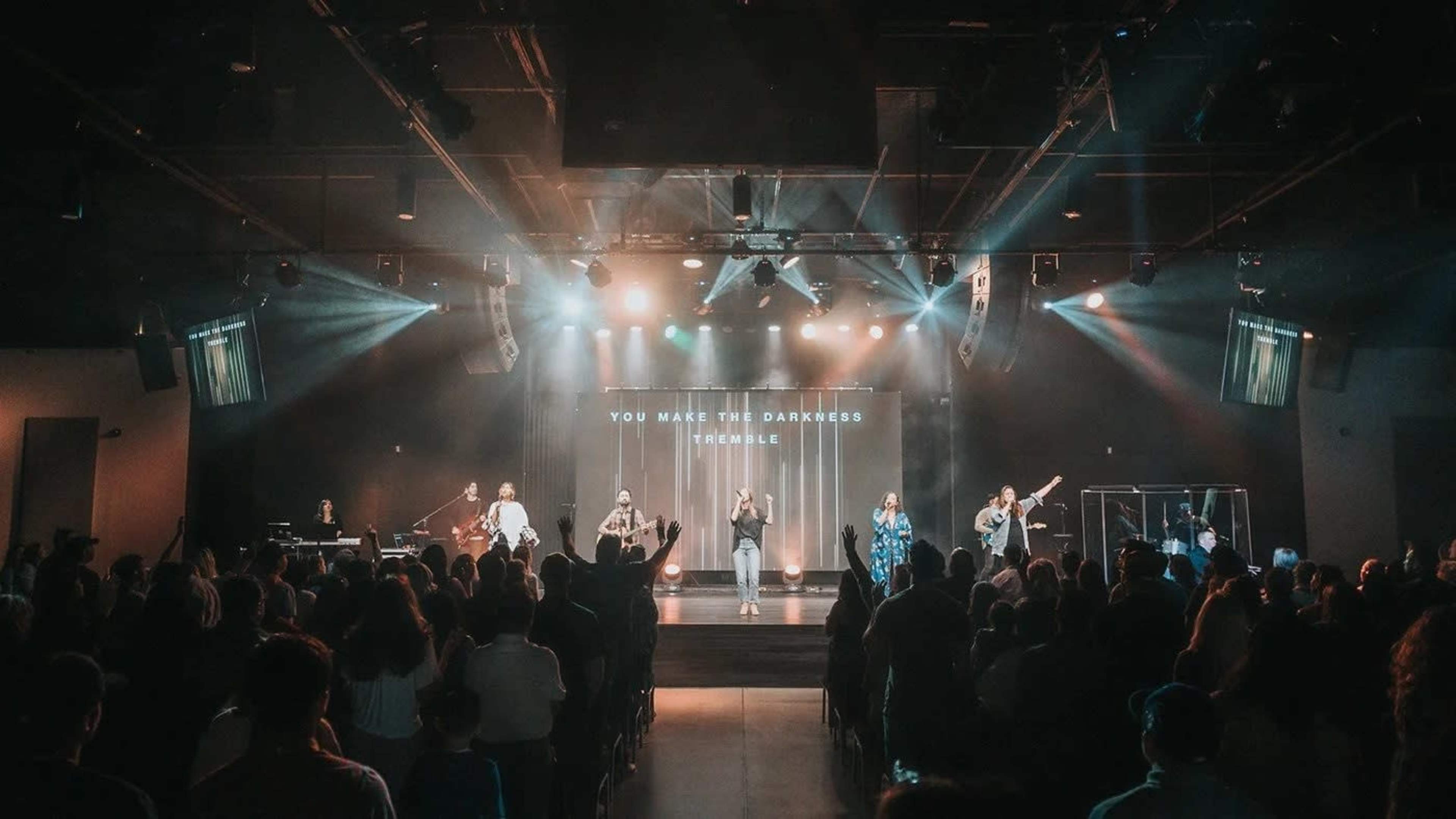A group of musicians performs on stage in front of an audience in a well-lit auditorium.