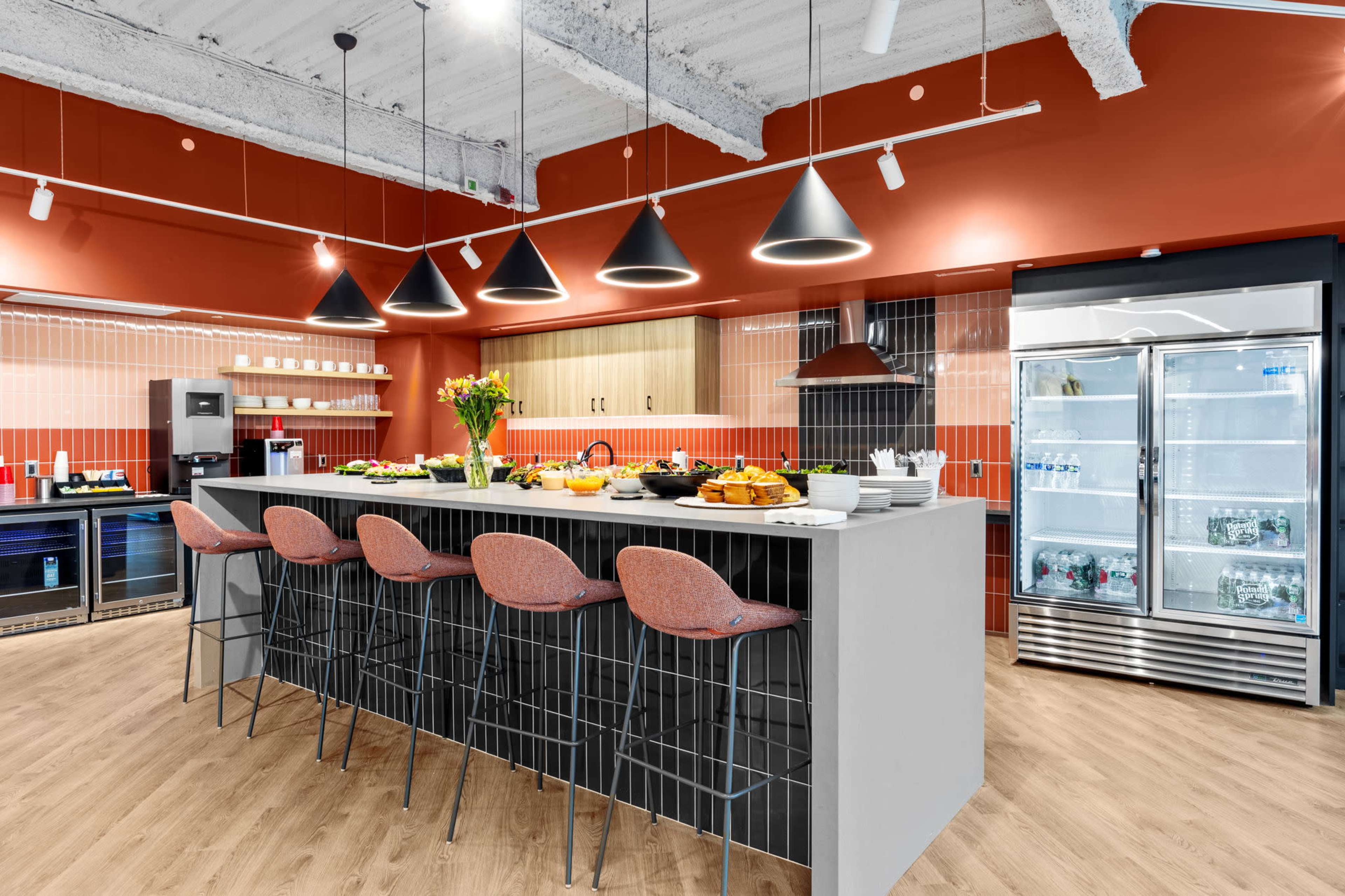 A modern kitchen features a central island with bar stools, a variety of fresh foods on display, and sleek appliances against a backdrop of contrasting wall colors.