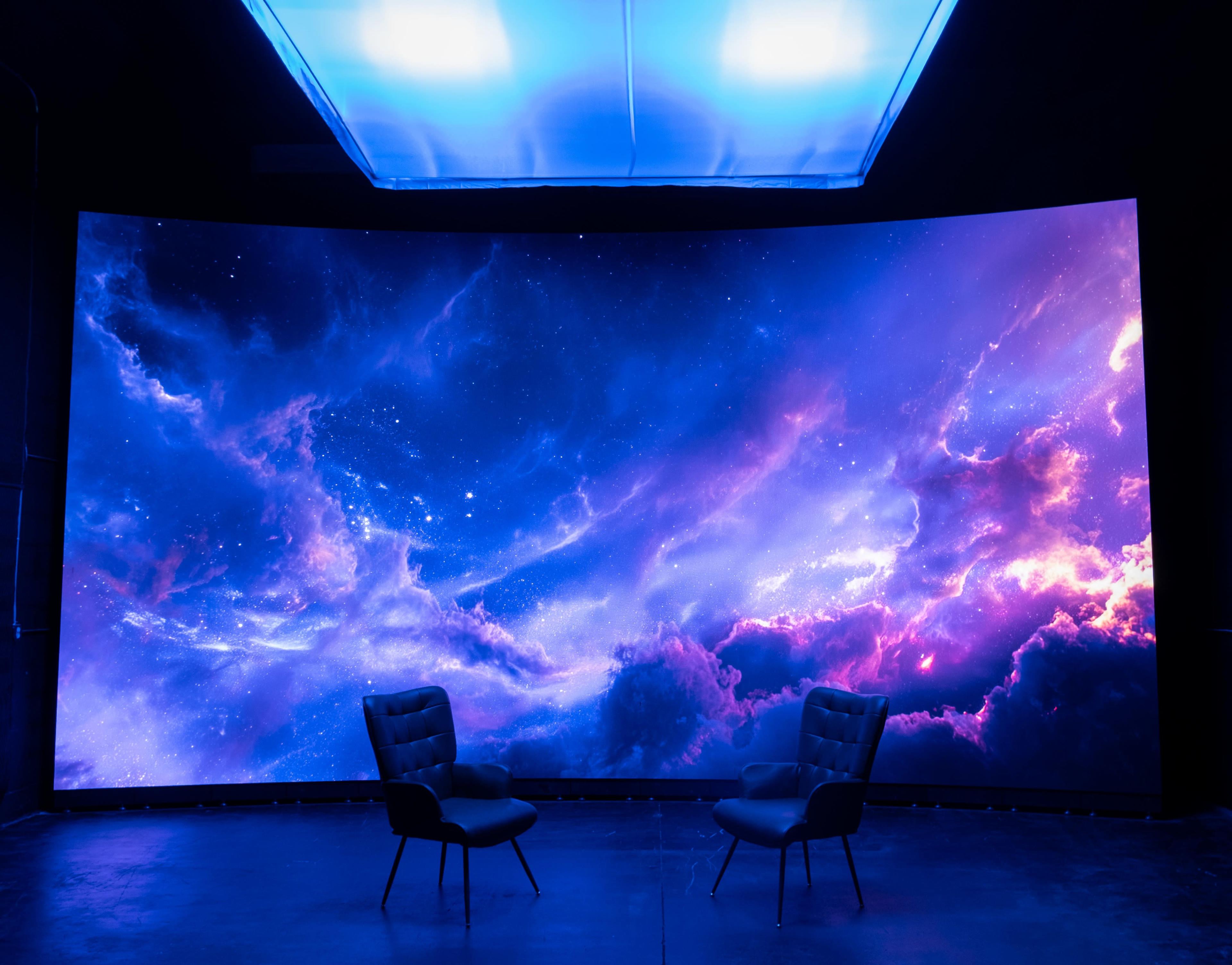 The image features two chairs placed in front of a large, curved screen displaying a colorful cosmic scene.