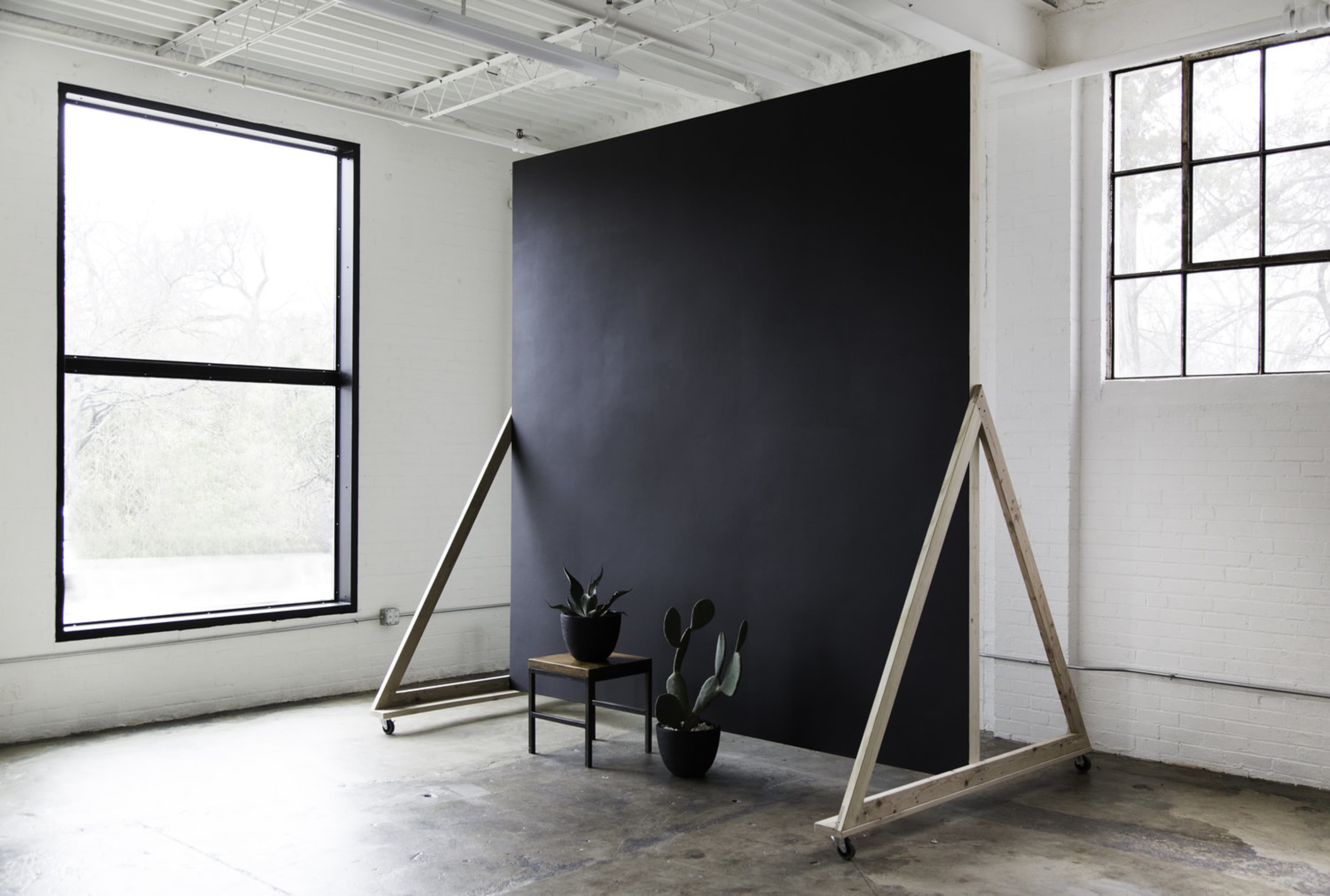 A minimalist interior space featuring a large black backdrop, a wooden chair, and two potted plants.