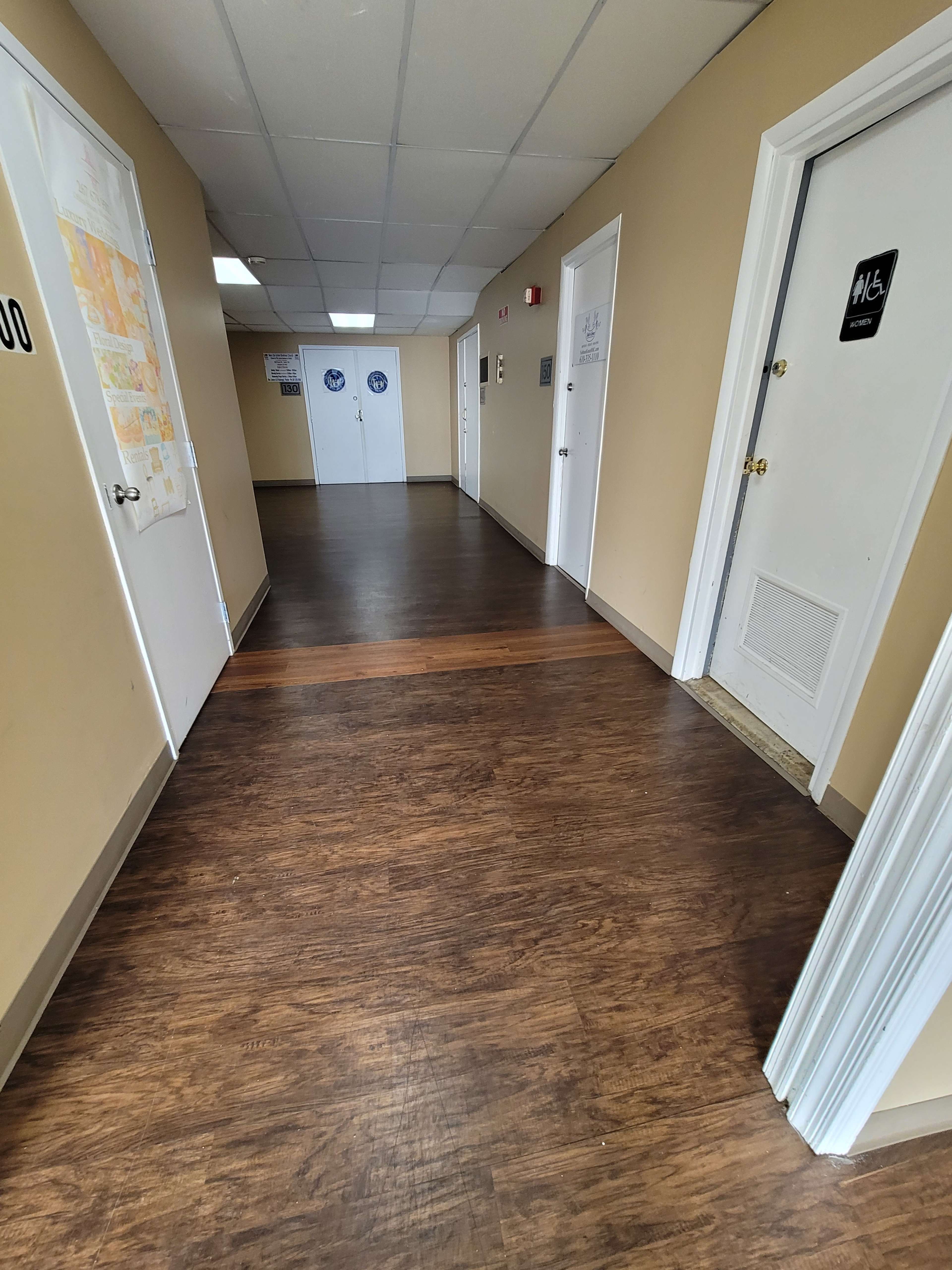 A long, narrow hallway with brown laminate flooring and several closed doors along the walls.
