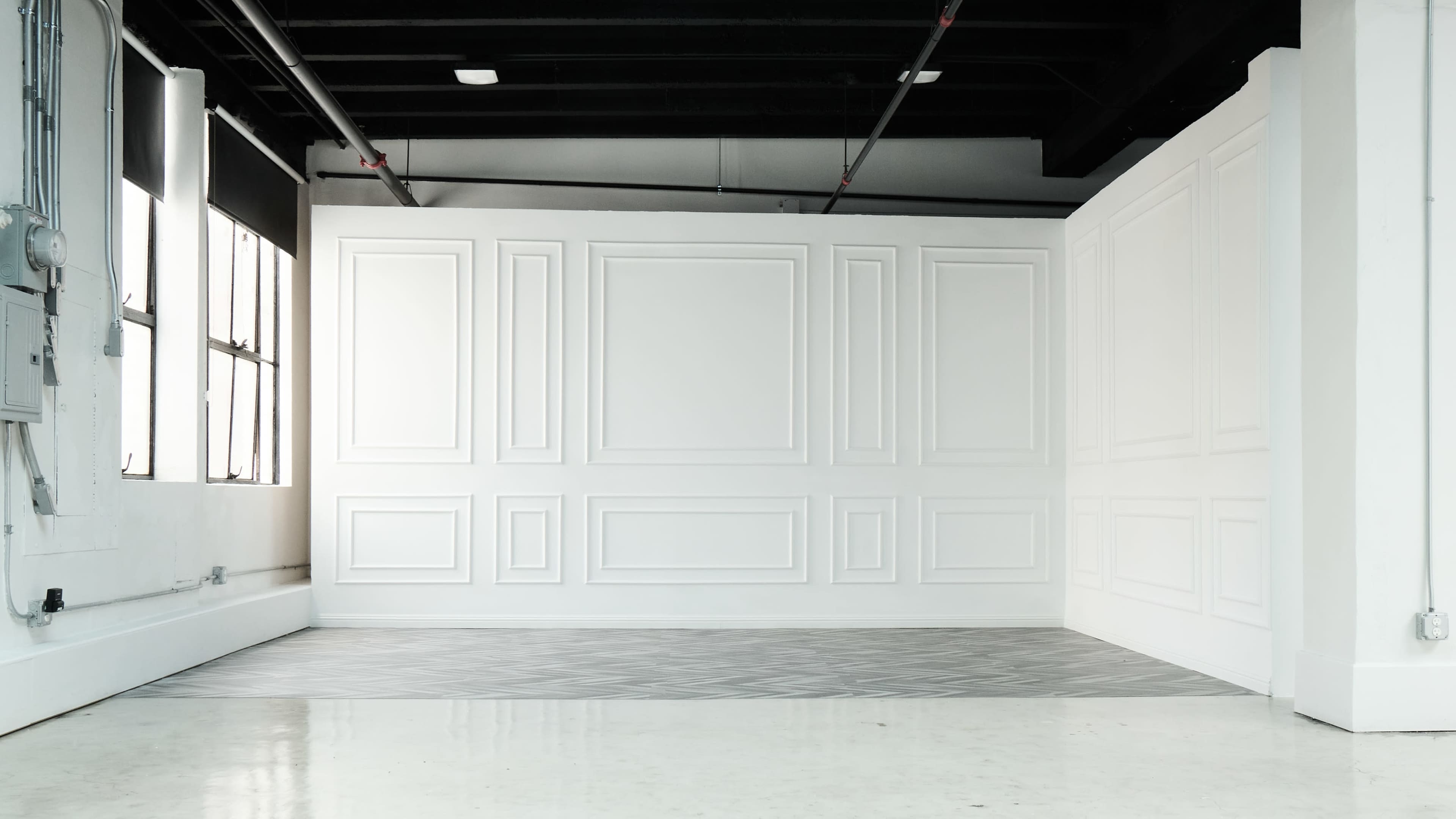 A spacious, minimalist room with a white paneled wall and a patterned floor.