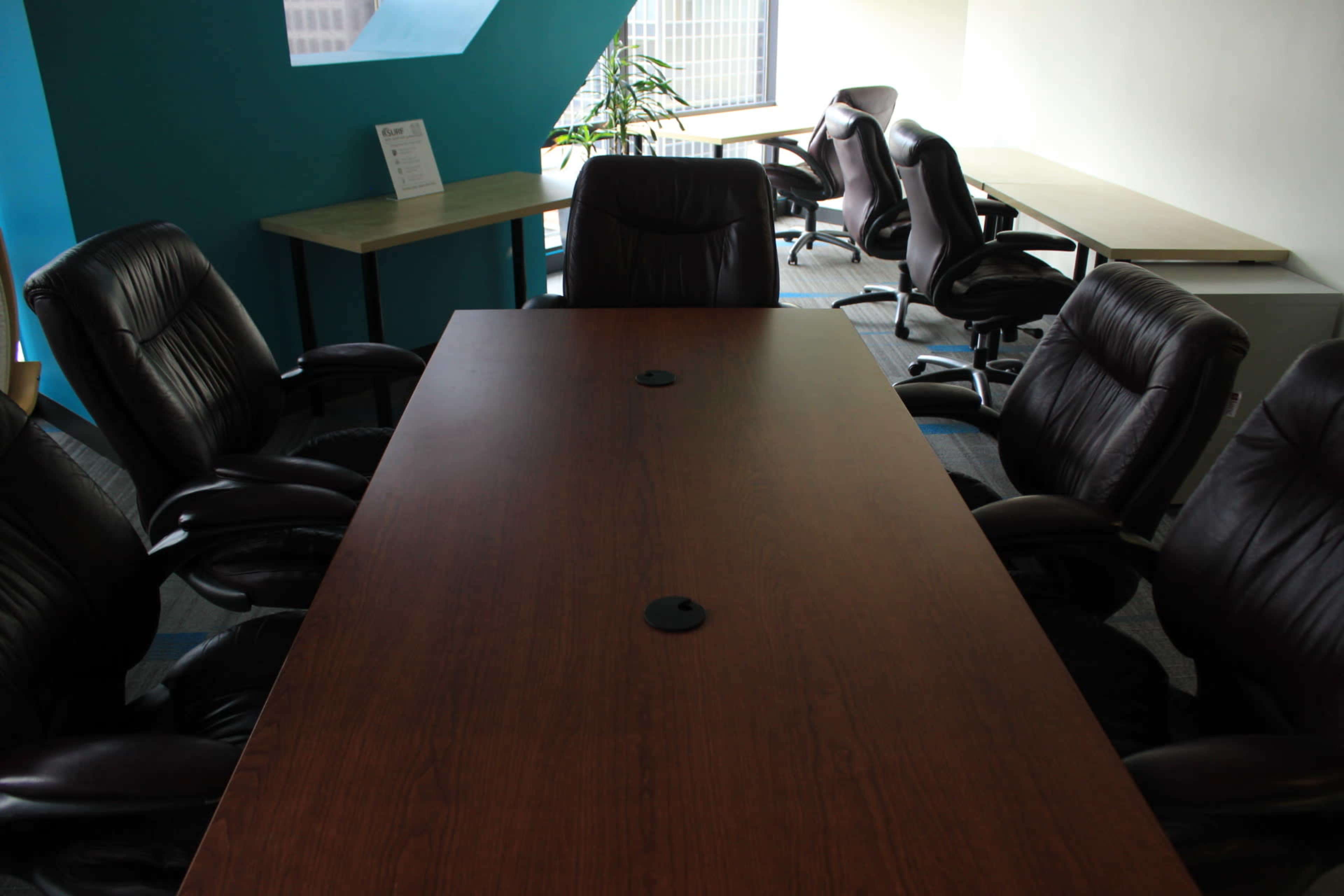 A large wooden conference table surrounded by several black office chairs in a bright, minimalistic meeting room.