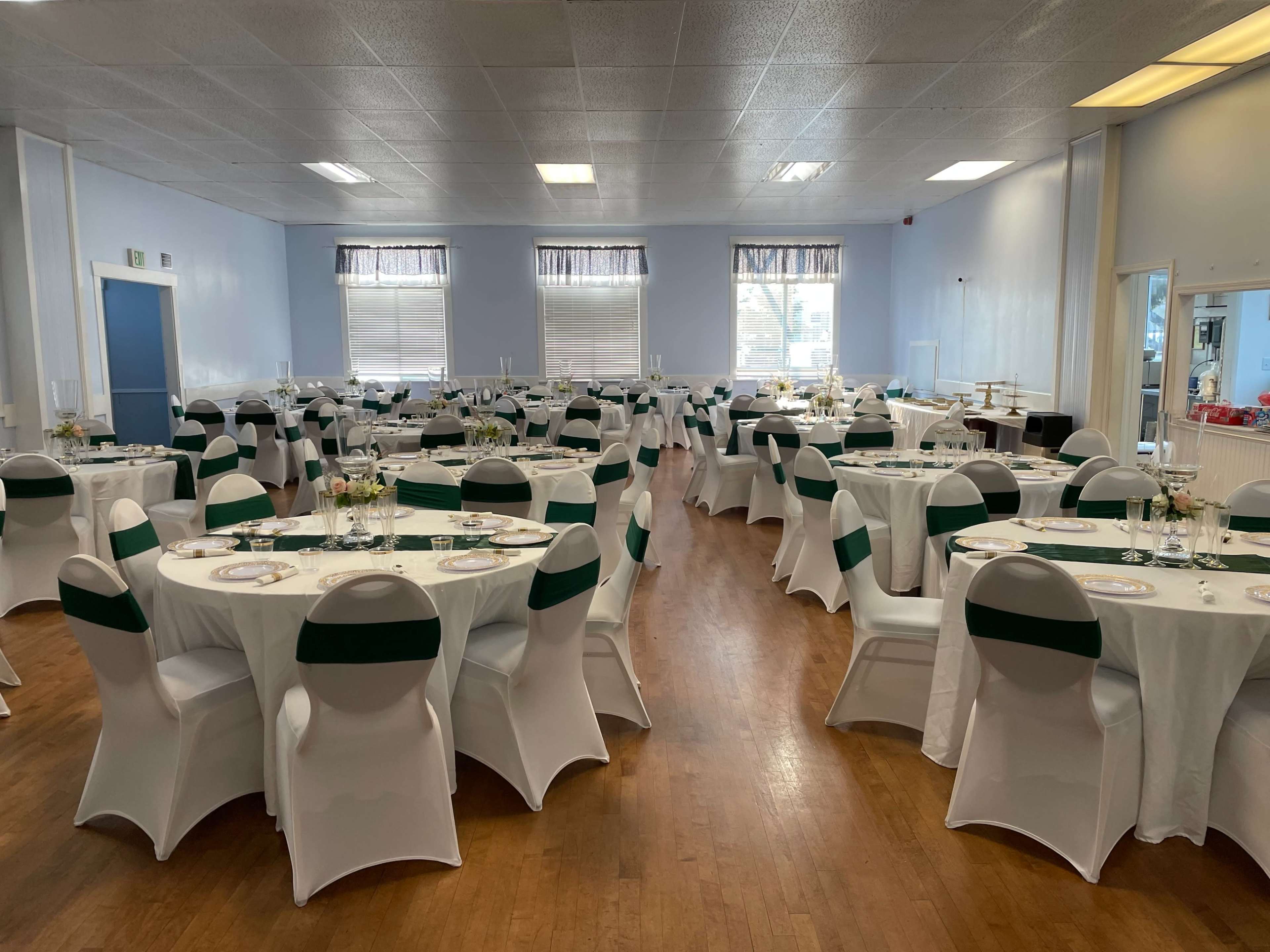 A large, elegantly arranged banquet hall with round tables covered in white tablecloths and dark green accents, set for an event.