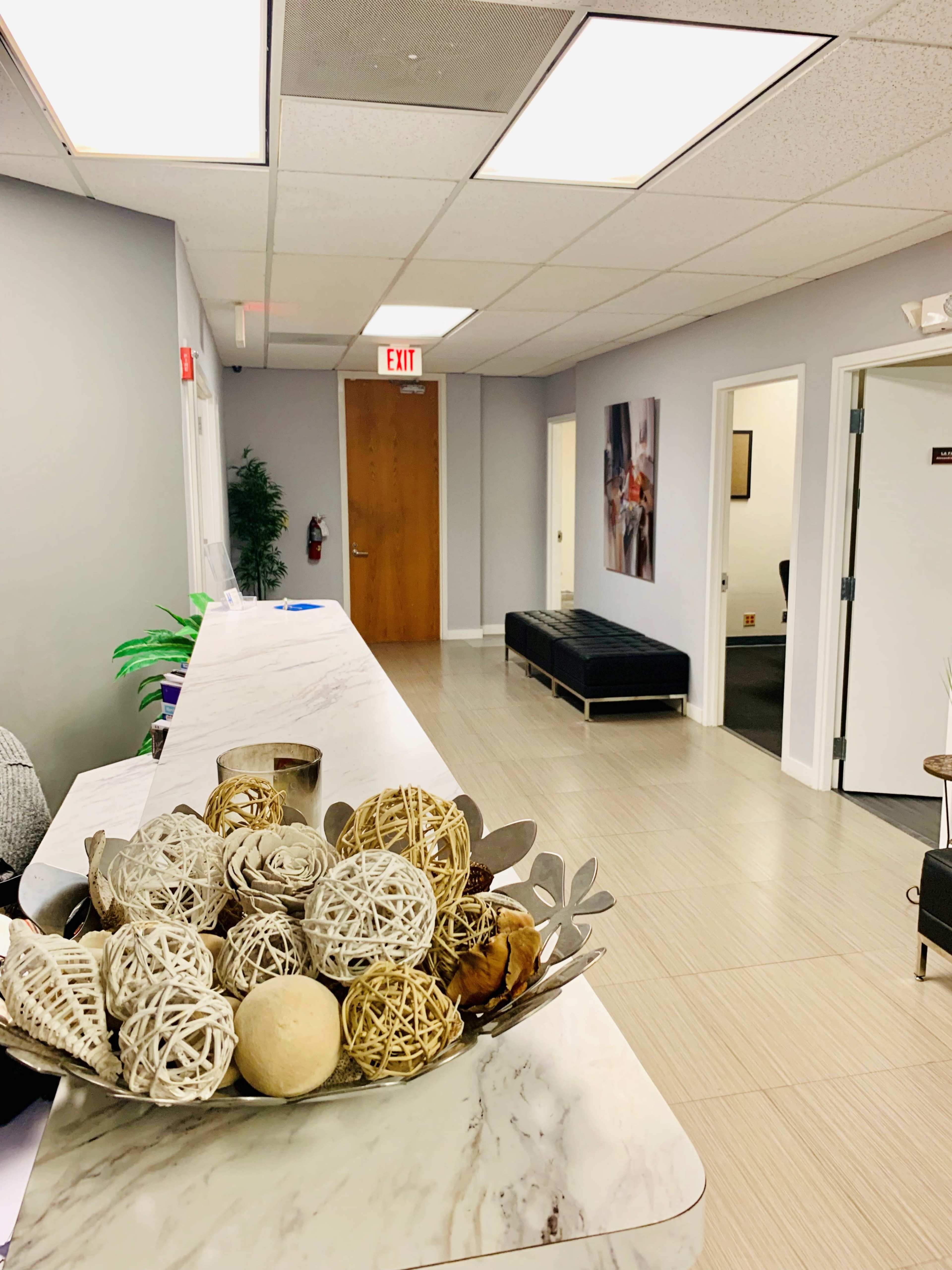 A marble reception desk sits in the foreground, with decorative orbs displayed in a bowl, while a well-lit hallway leads to multiple office doors in the background.