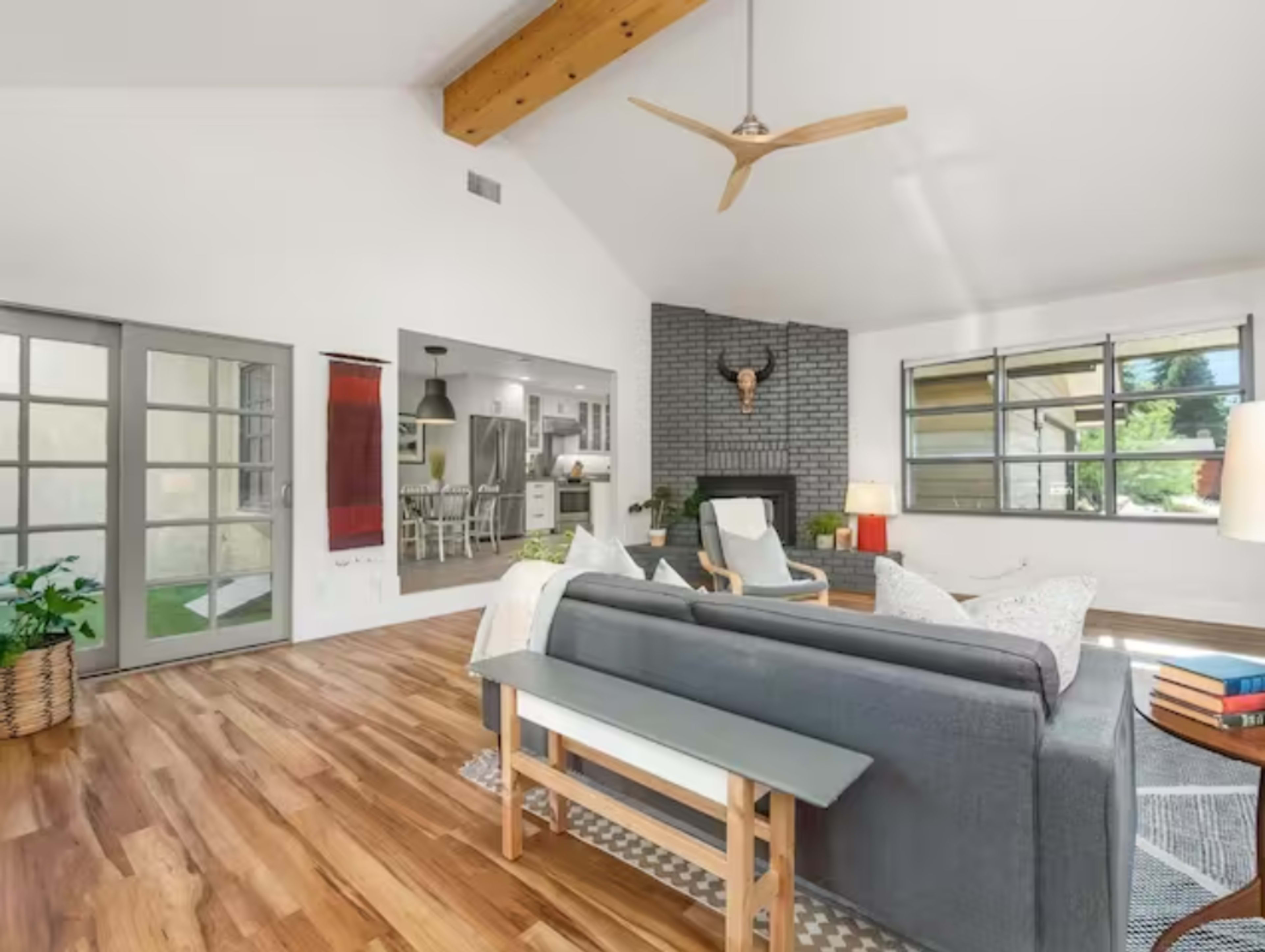 A bright, modern living room featuring a gray sofa, wooden flooring, and a decorative fireplace with a mounted antler display.