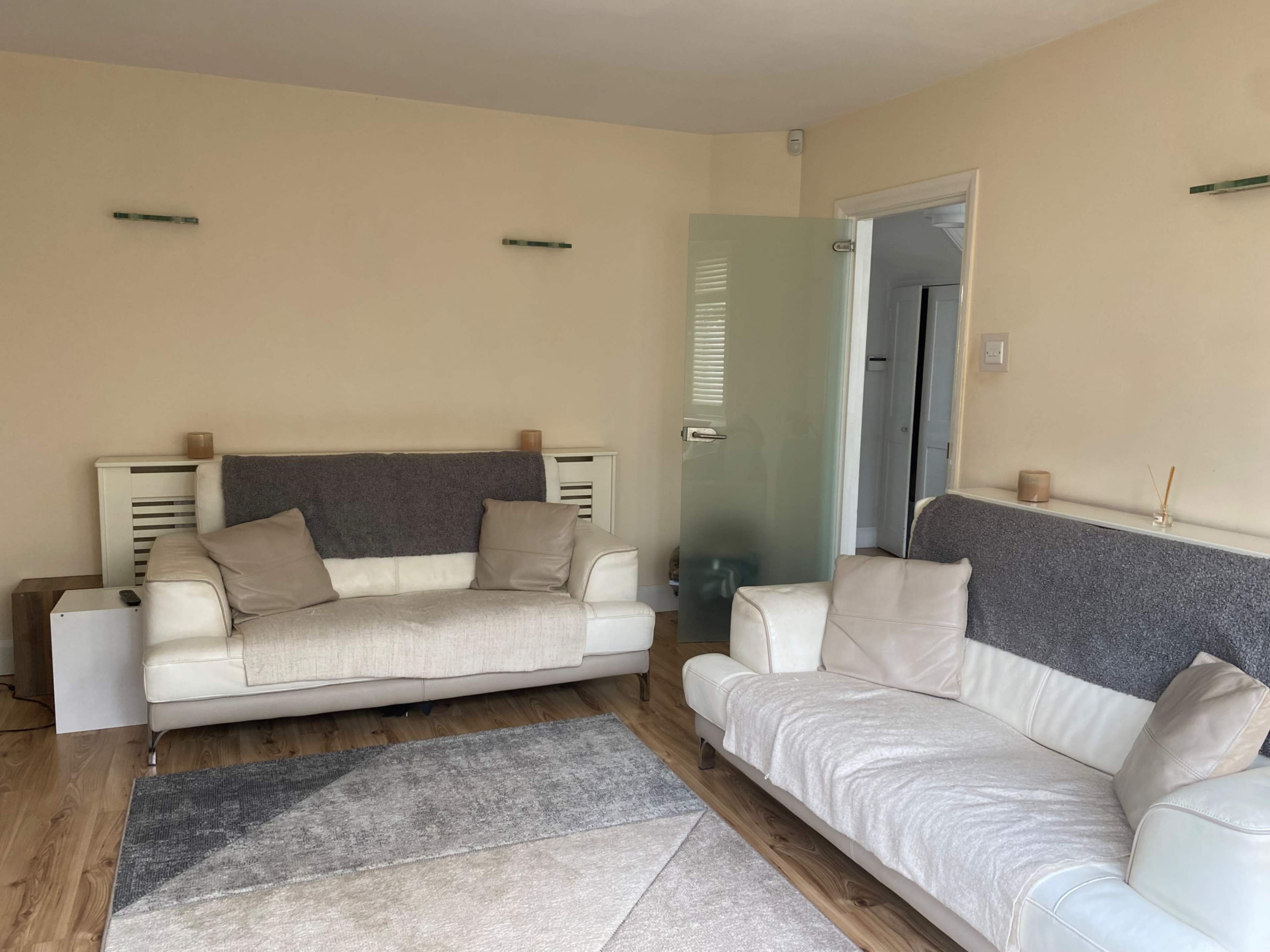 The image shows a living room with two sofas, a light-colored rug, and a glass door leading to another room.