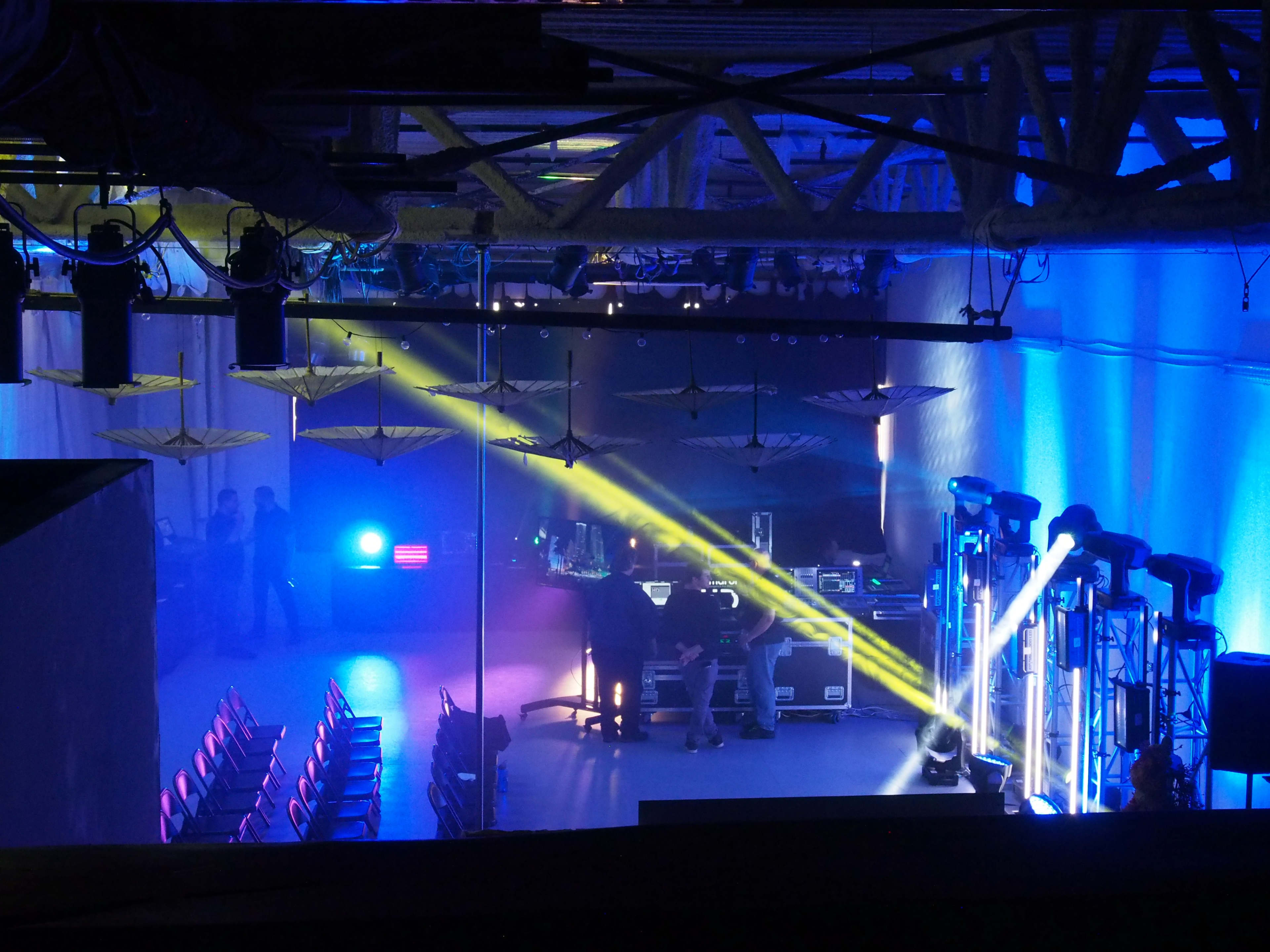 A spacious event venue with rows of empty chairs and colorful stage lighting being set up for an upcoming performance.