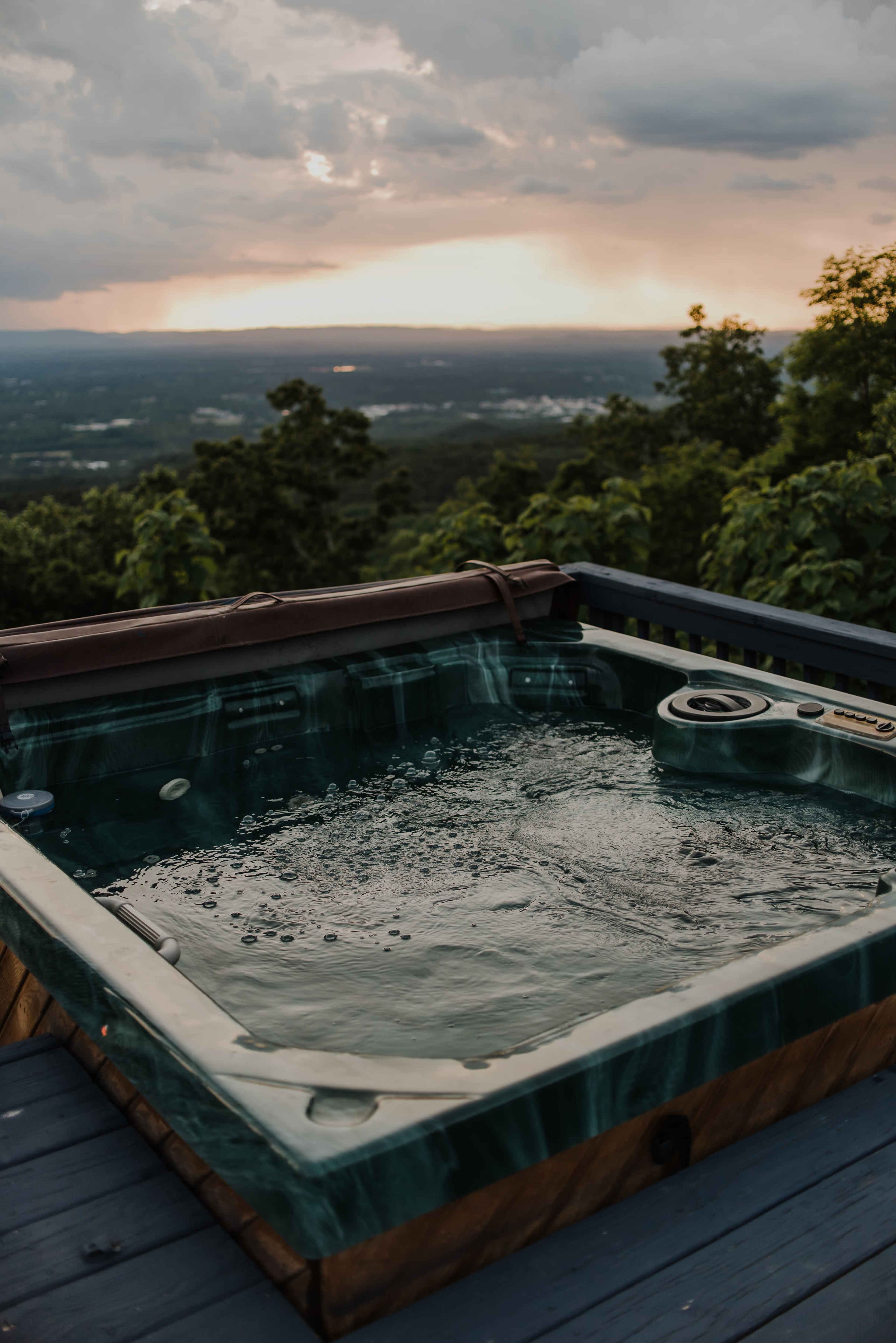 A hot tub filled with bubbling water overlooks a valley and distant mountains under a cloudy sky.