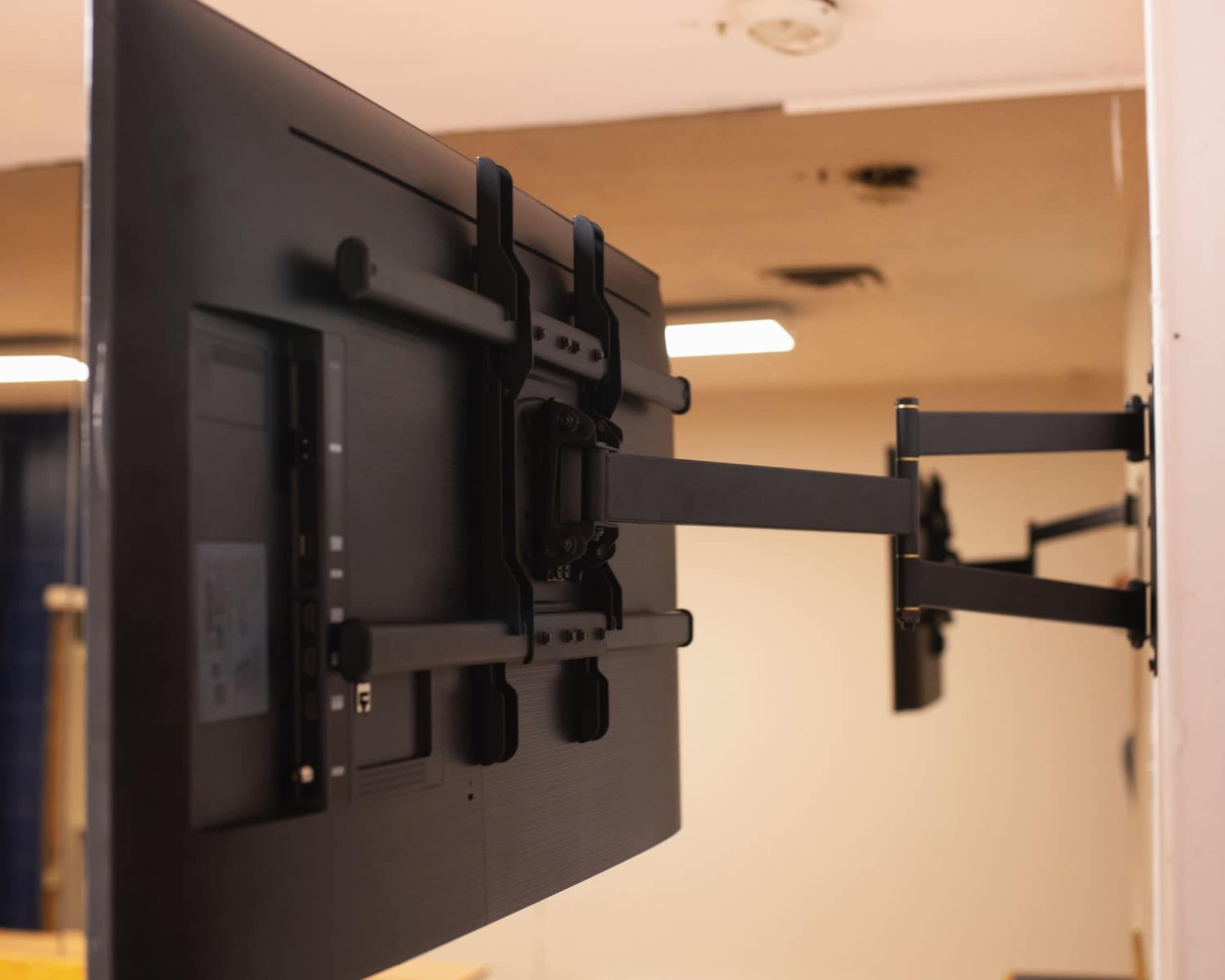 A flat-screen television is mounted on a wall with an adjustable arm bracket for positioning.