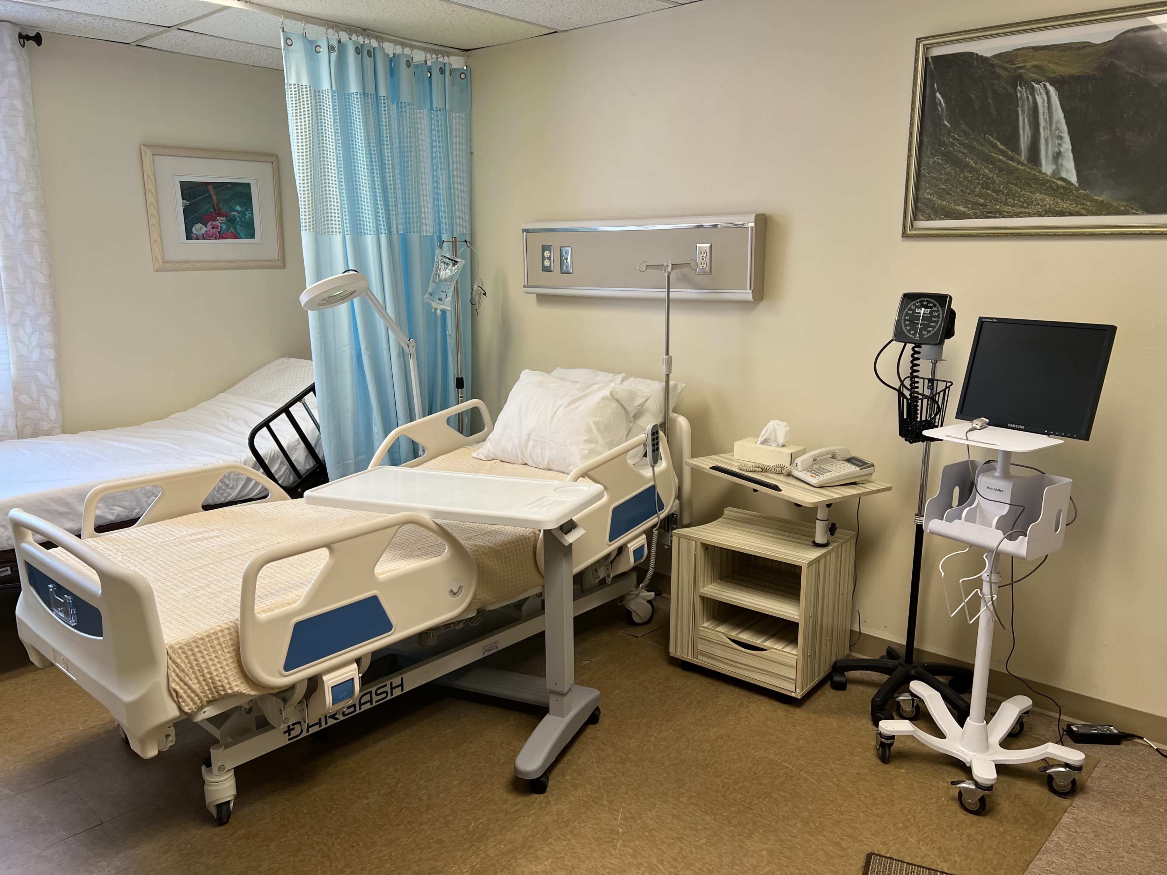 The image shows a hospital room with two beds, medical equipment, and a computer workstation.