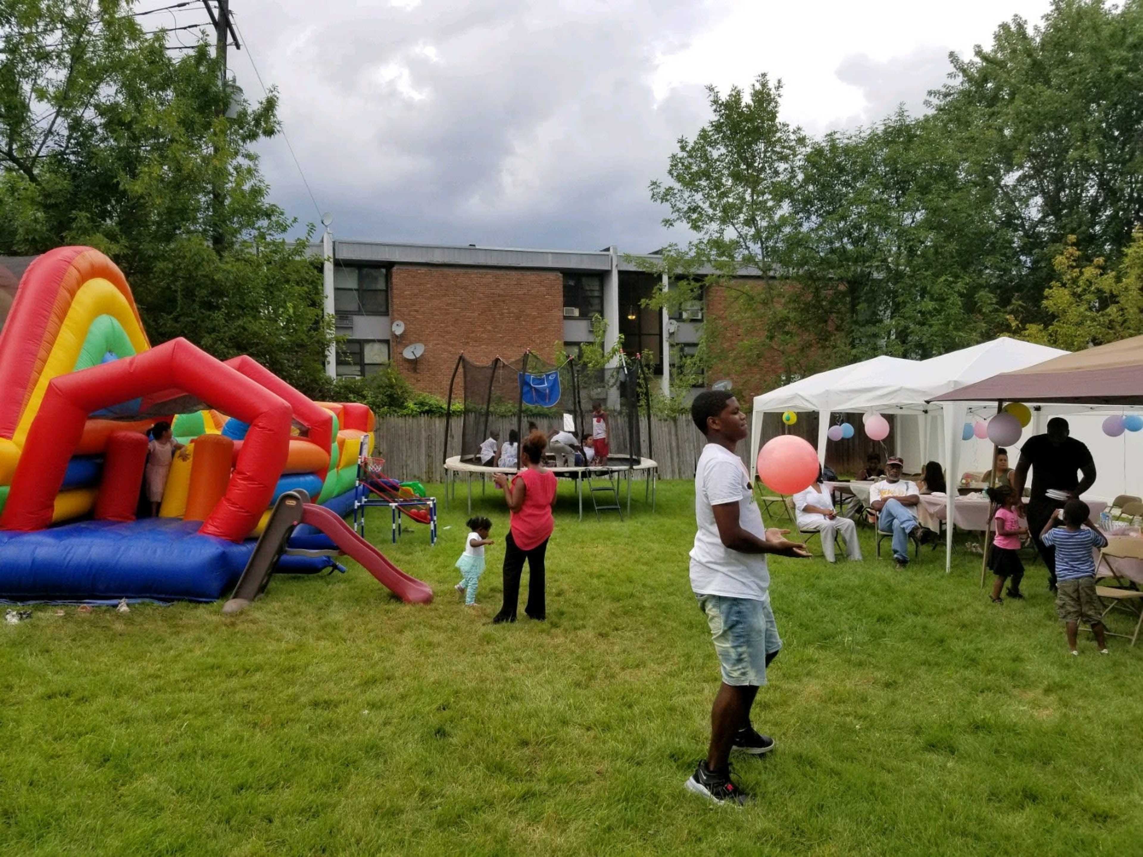 A man juggles a balloon near a bouncy castle and tents set up for a celebration in a grassy area.