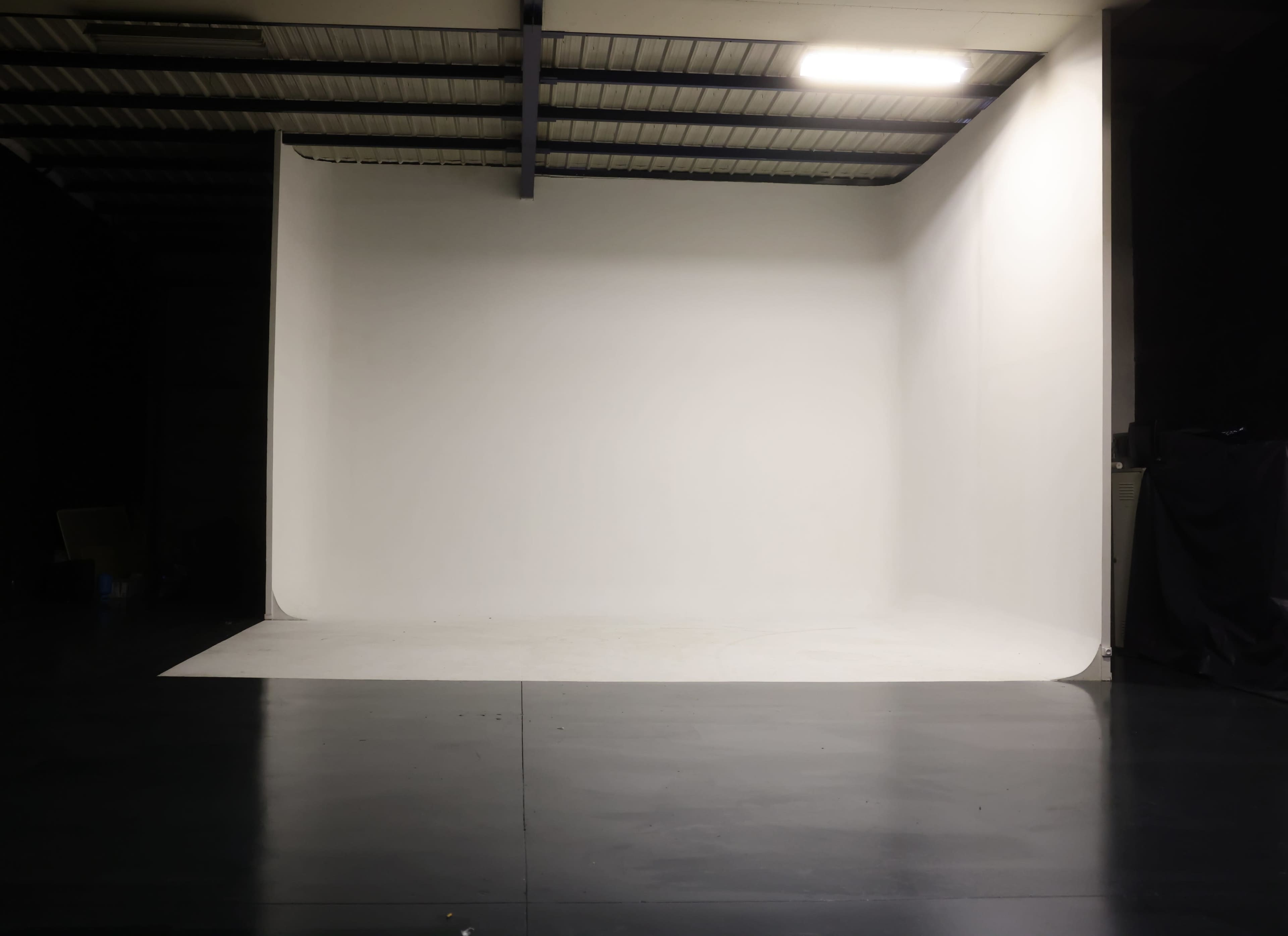 A spacious photography studio with a large seamless white backdrop and a polished dark floor.
