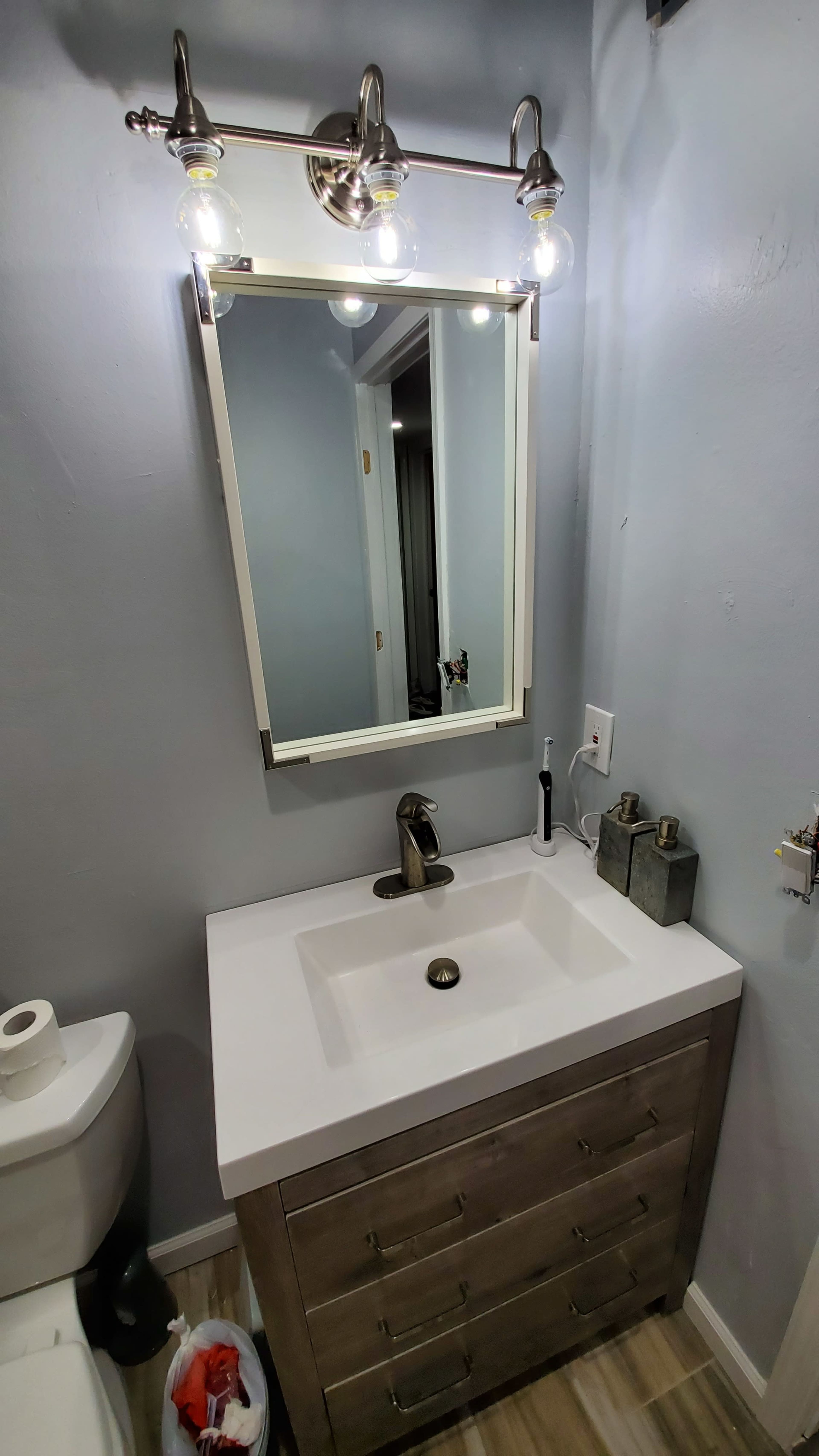 A modern bathroom with a sleek vanity featuring a white sink and a large mirror illuminated by three light fixtures above it.