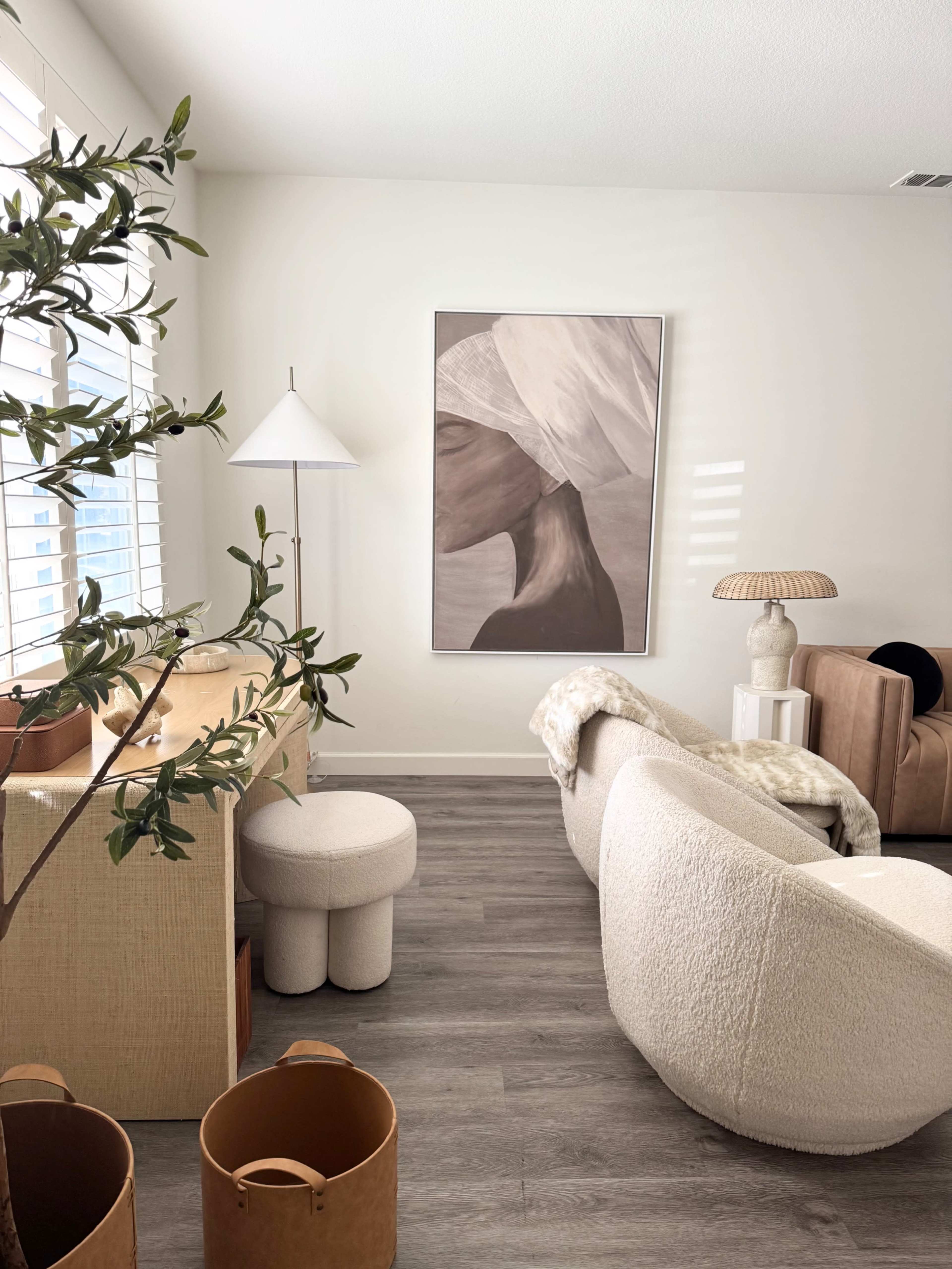 The image depicts a modern living room with a large artwork on the wall, a lamp, and various furniture pieces arranged around a wooden side table.