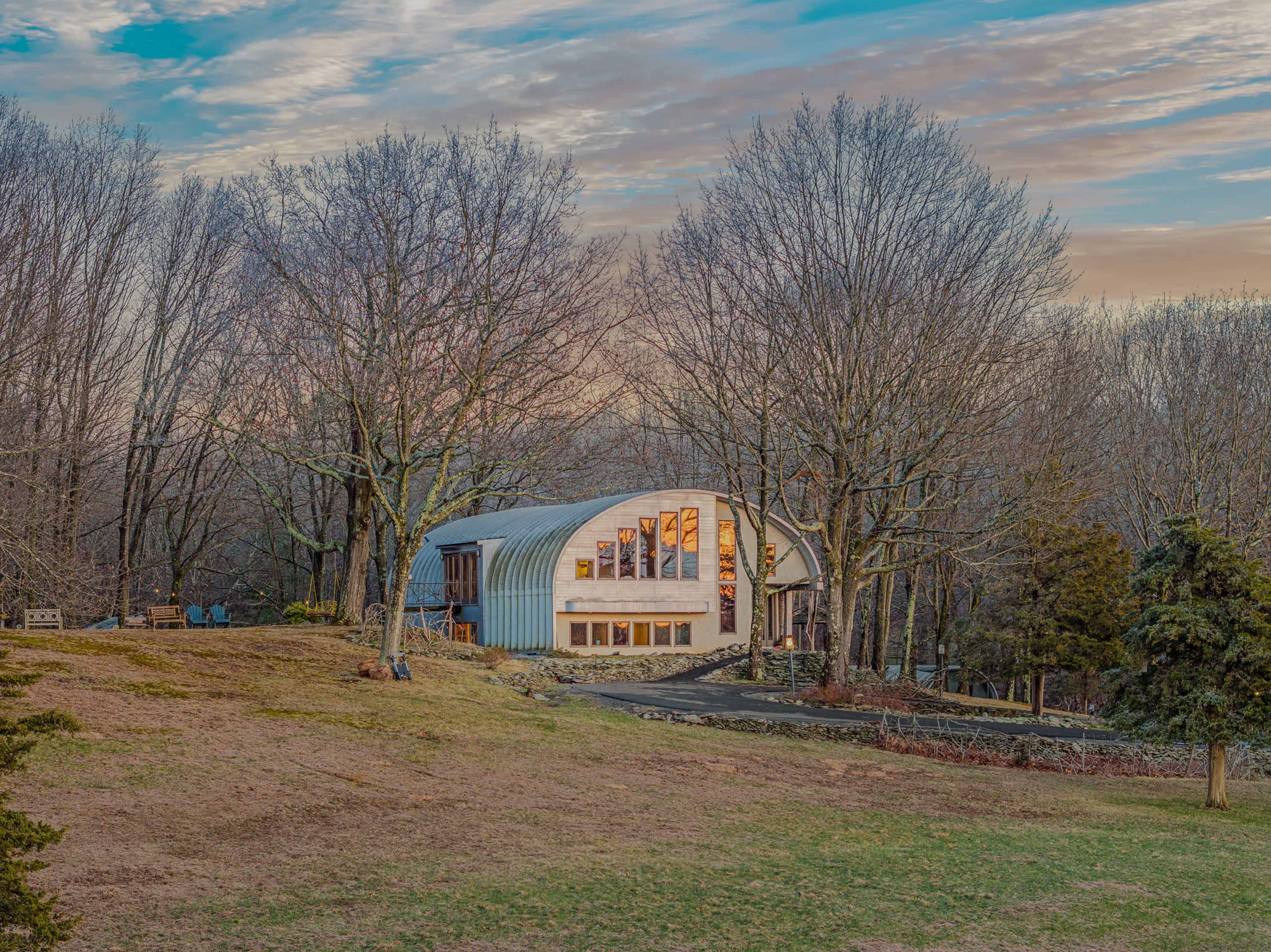 A modern barn-style structure with large windows is surrounded by leafless trees and a grassy area.