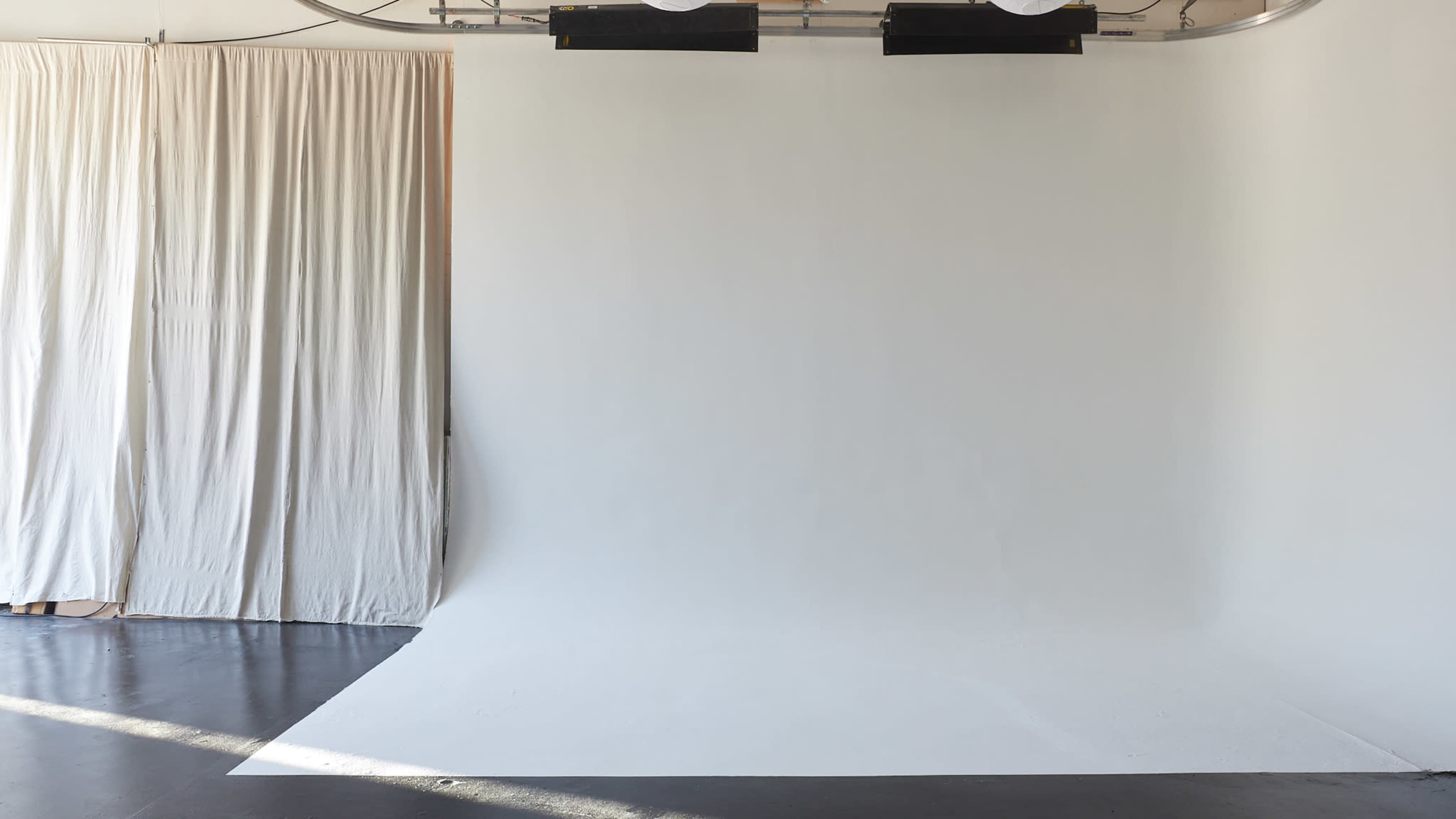 The image shows a spacious studio with a white backdrop and curtains on one side.