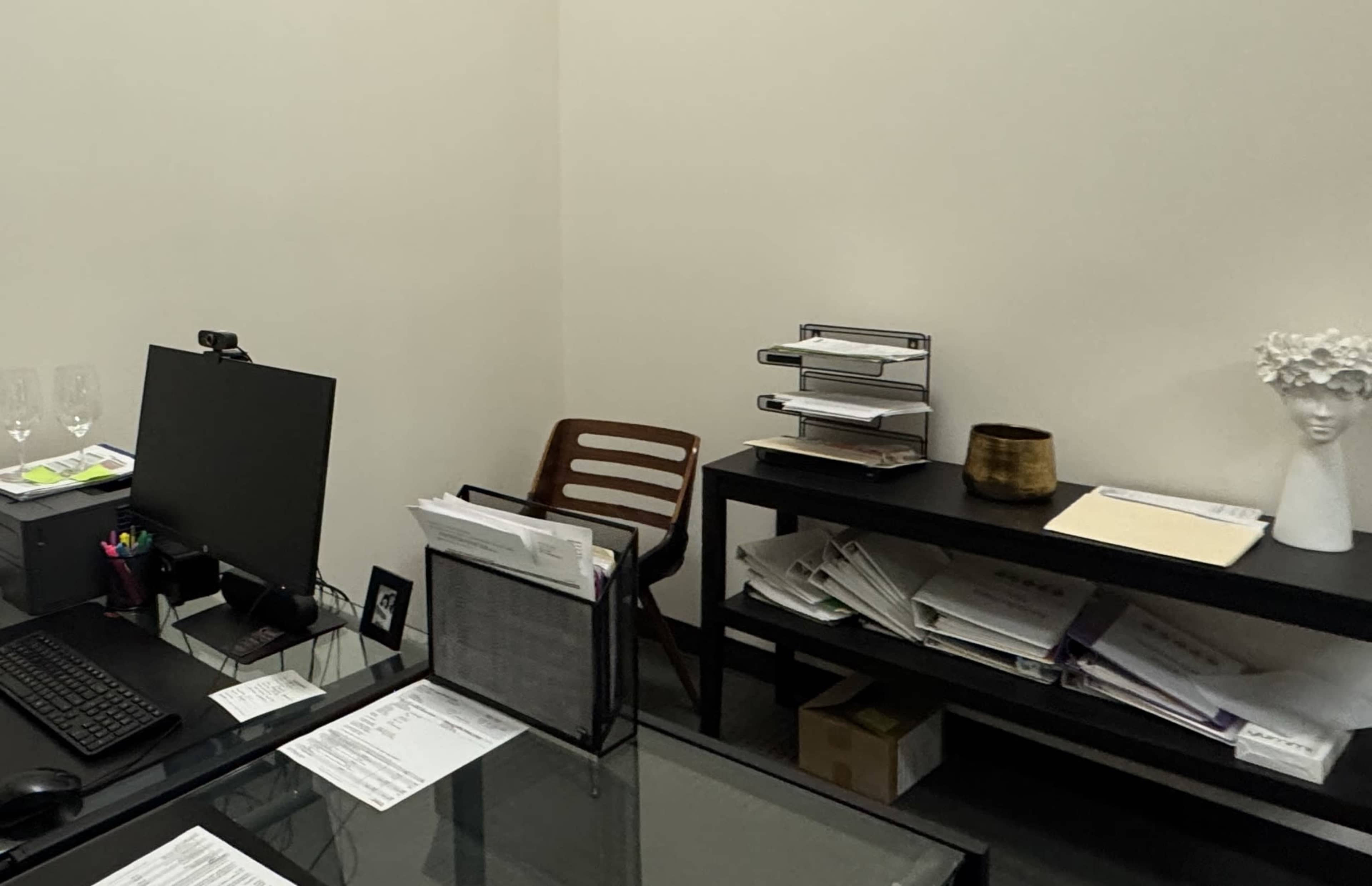 The image shows a workspace with a computer monitor, a wooden chair, and a shelf holding several binders and a decorative object.