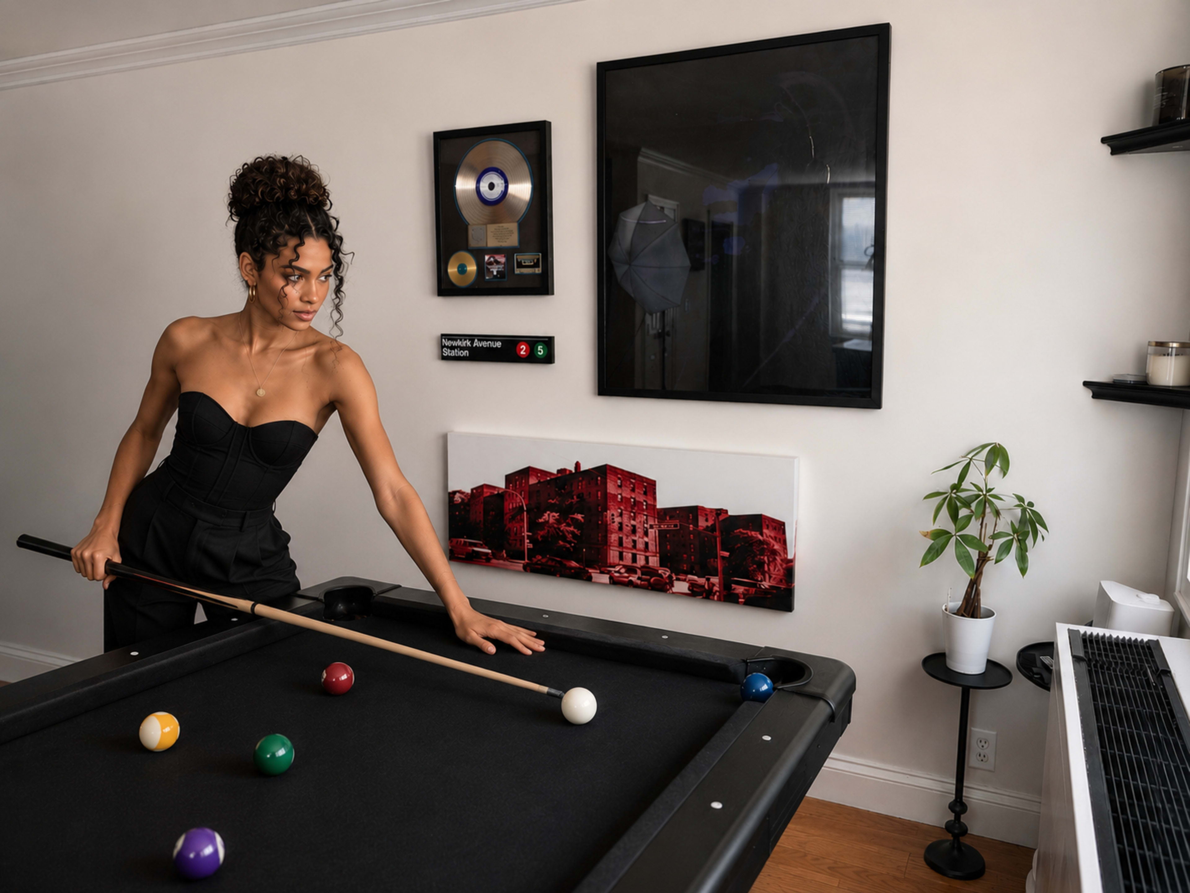A woman in a black outfit is playing pool at a table in a brightly lit room with framed artwork on the walls.
