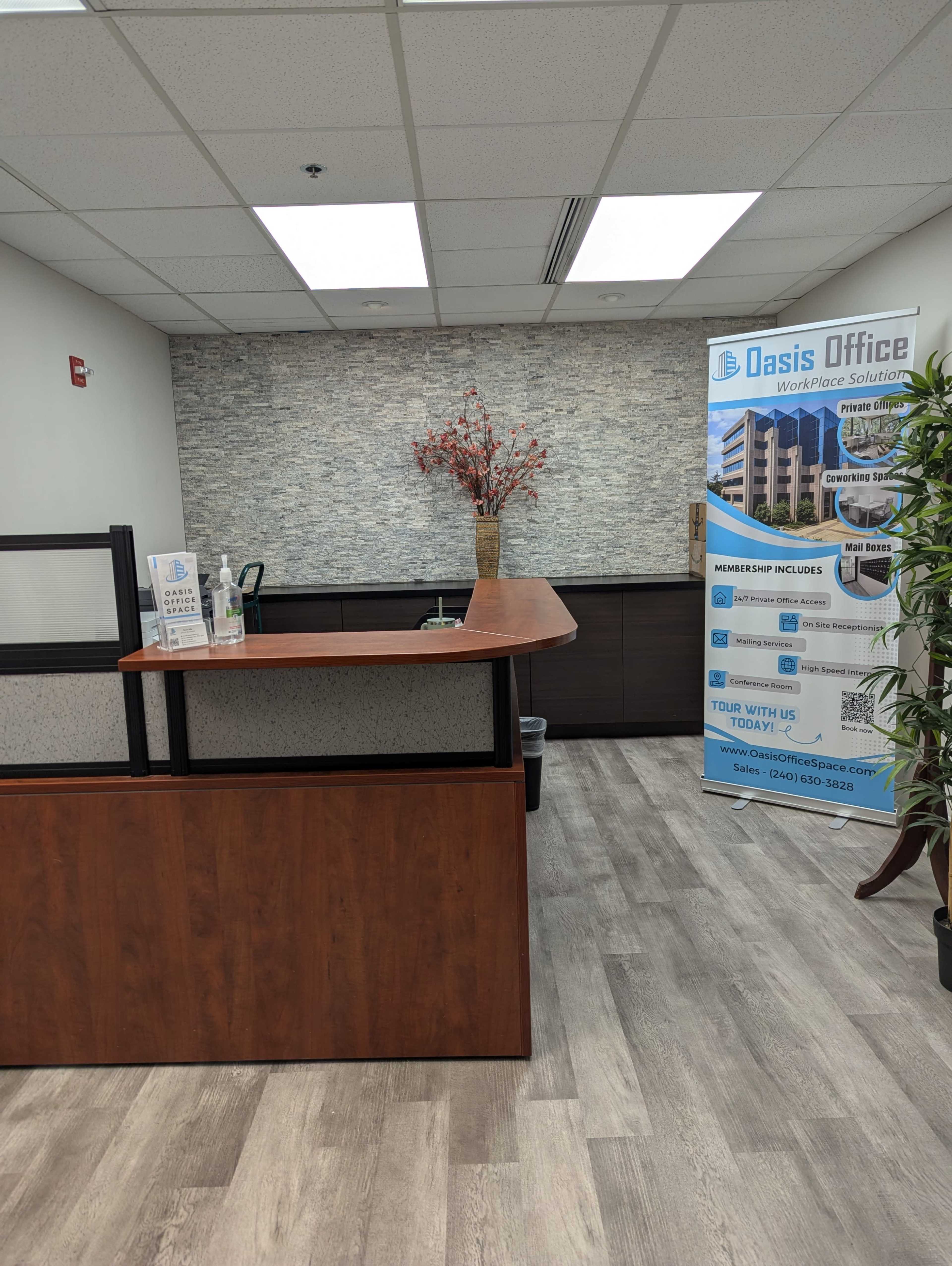 The image shows a modern office reception area with a wooden reception desk, decorative plant, and informational banner on the side.