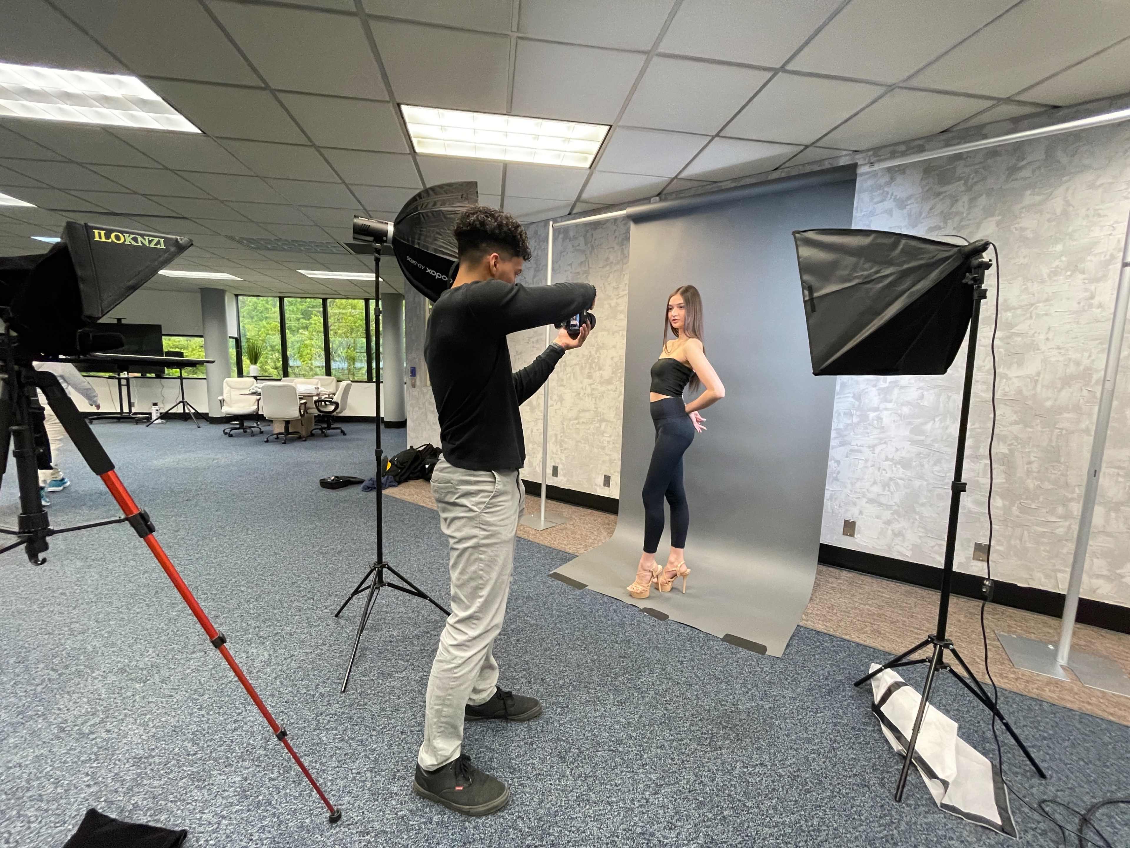 A photographer captures a model posing in front of a backdrop in a spacious studio.