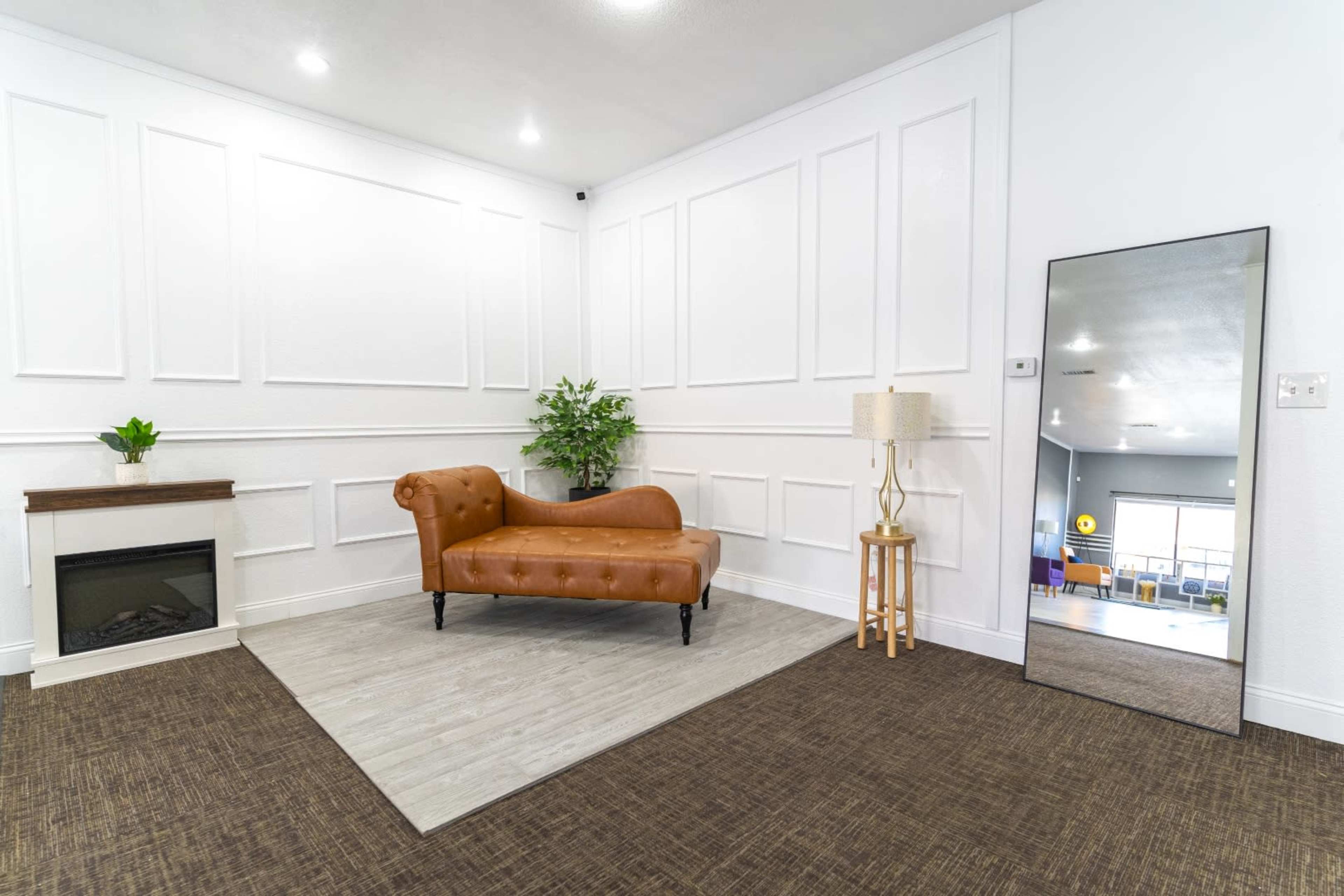 The image shows a room with a brown leather sofa, a decorative plant, a standing lamp, and a large mirror against a wall with paneling, along with a textured carpet floor.