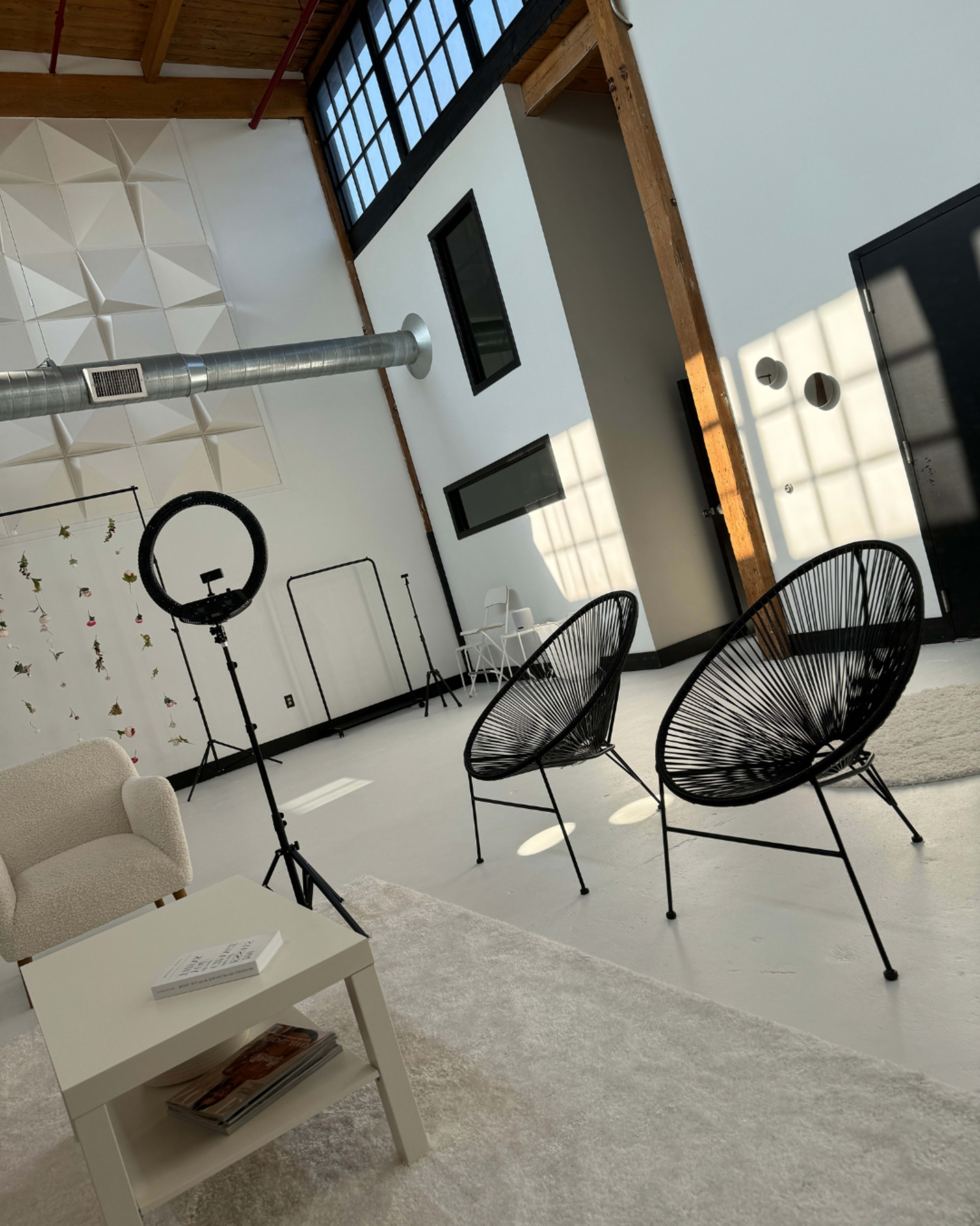 A bright, modern interior featuring two black wire chairs, a white table, and large windows.