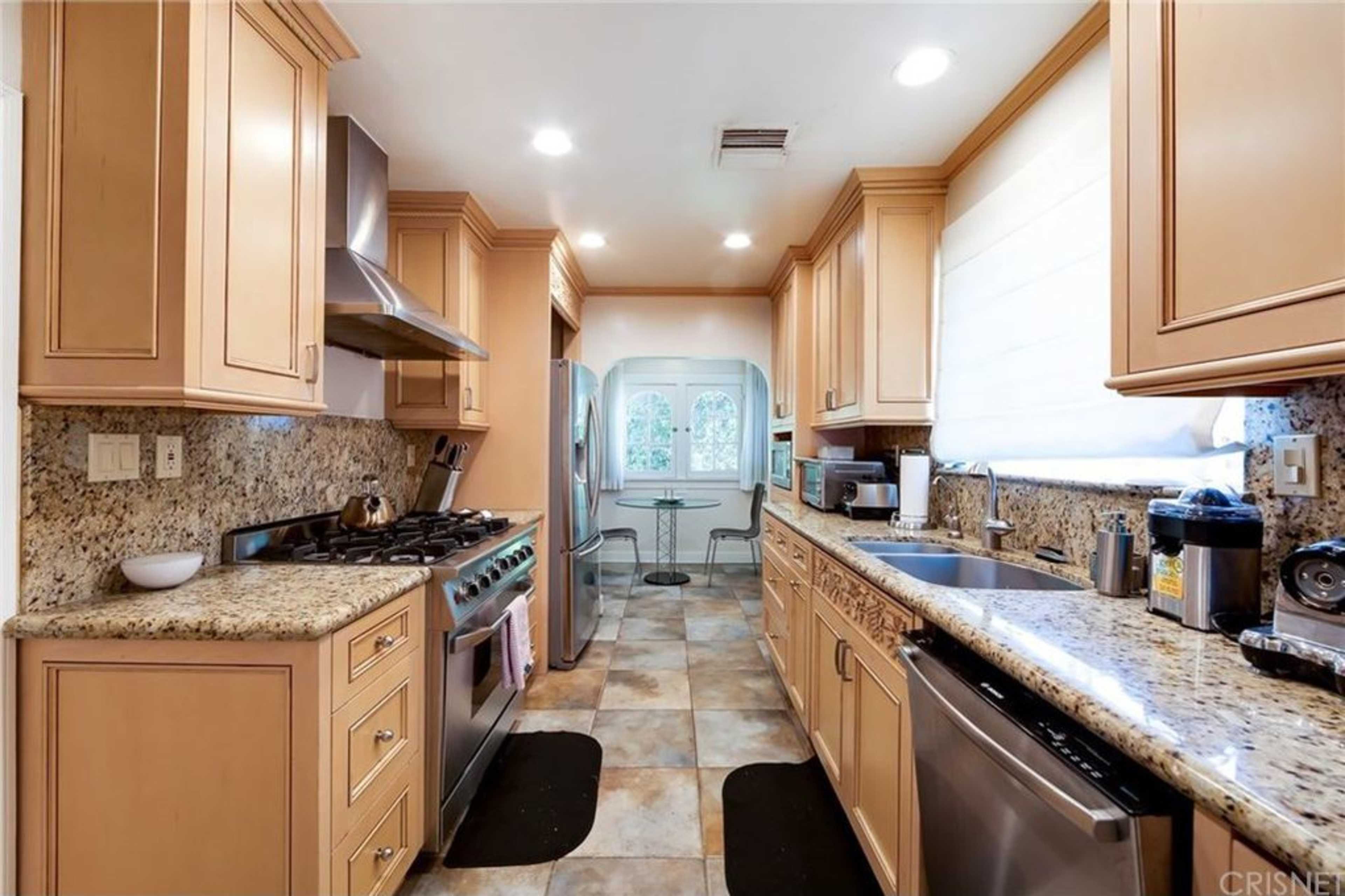 The kitchen features light wood cabinetry, granite countertops, and stainless steel appliances, with a window overlooking an outdoor area.
