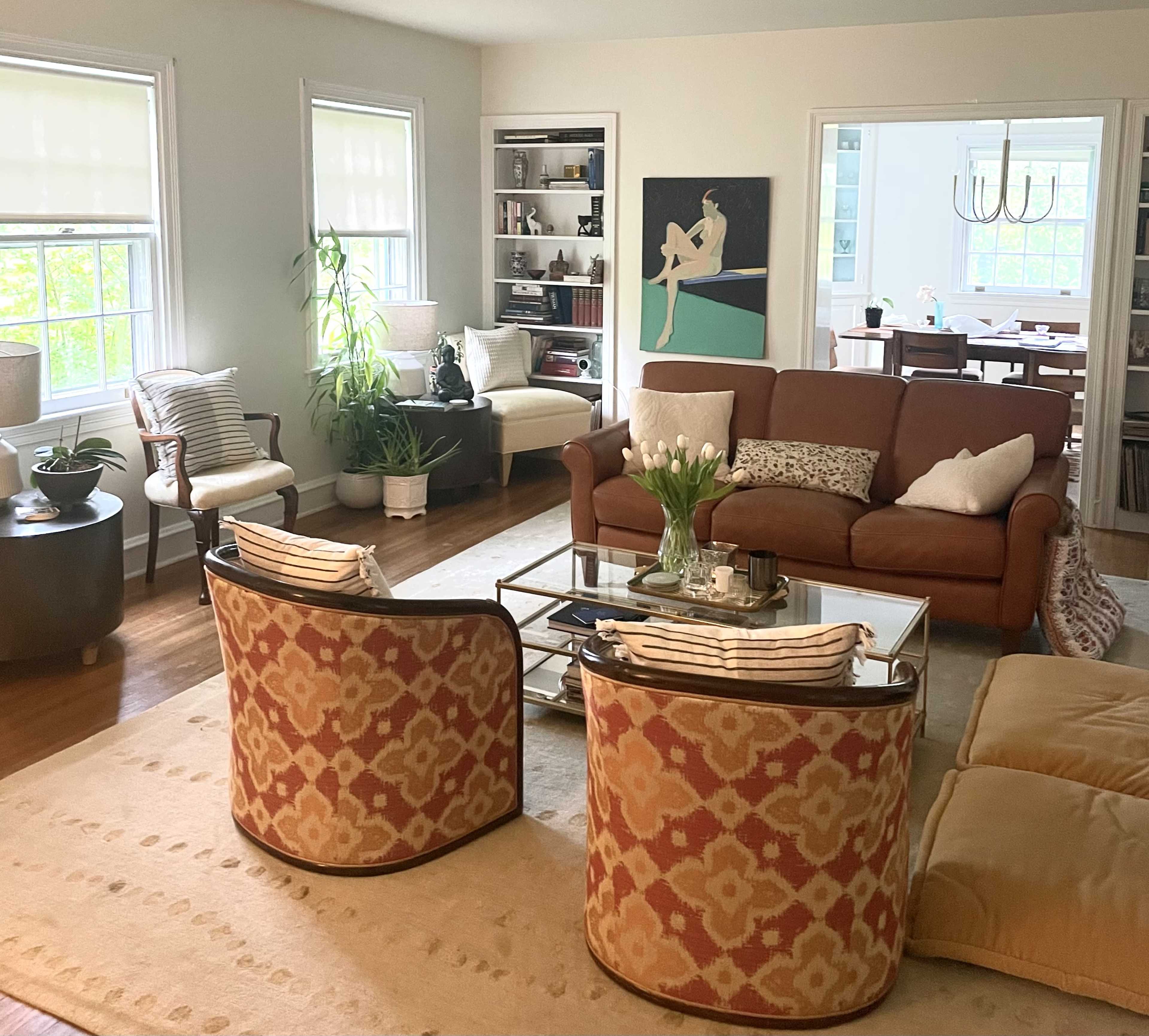 A bright living room with a brown sofa, two patterned chairs, a coffee table, and large windows allowing natural light.